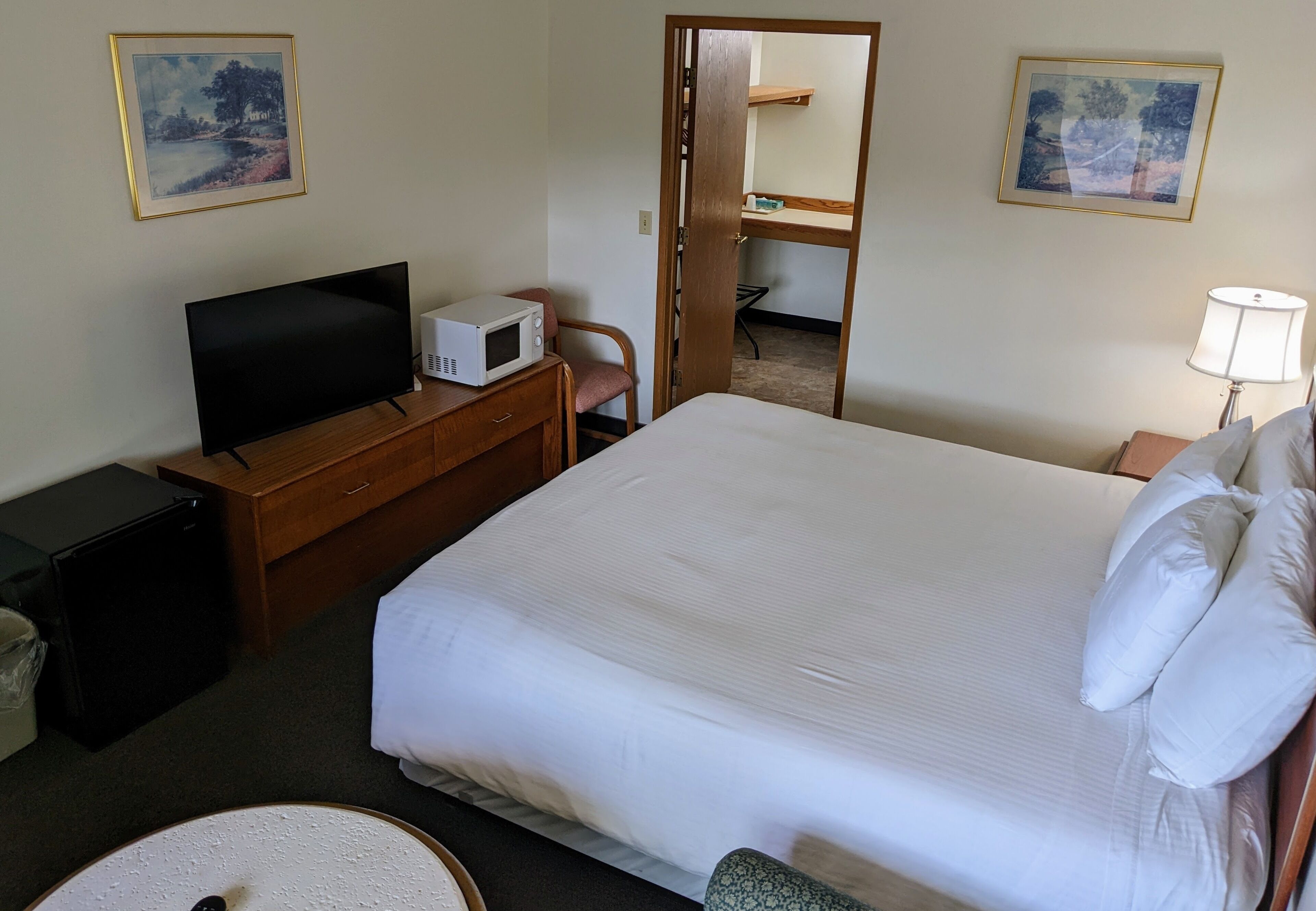 A hotel room with a bed, a television, a microwave, a desk, a chair, a lamp, and two framed pictures on the walls.