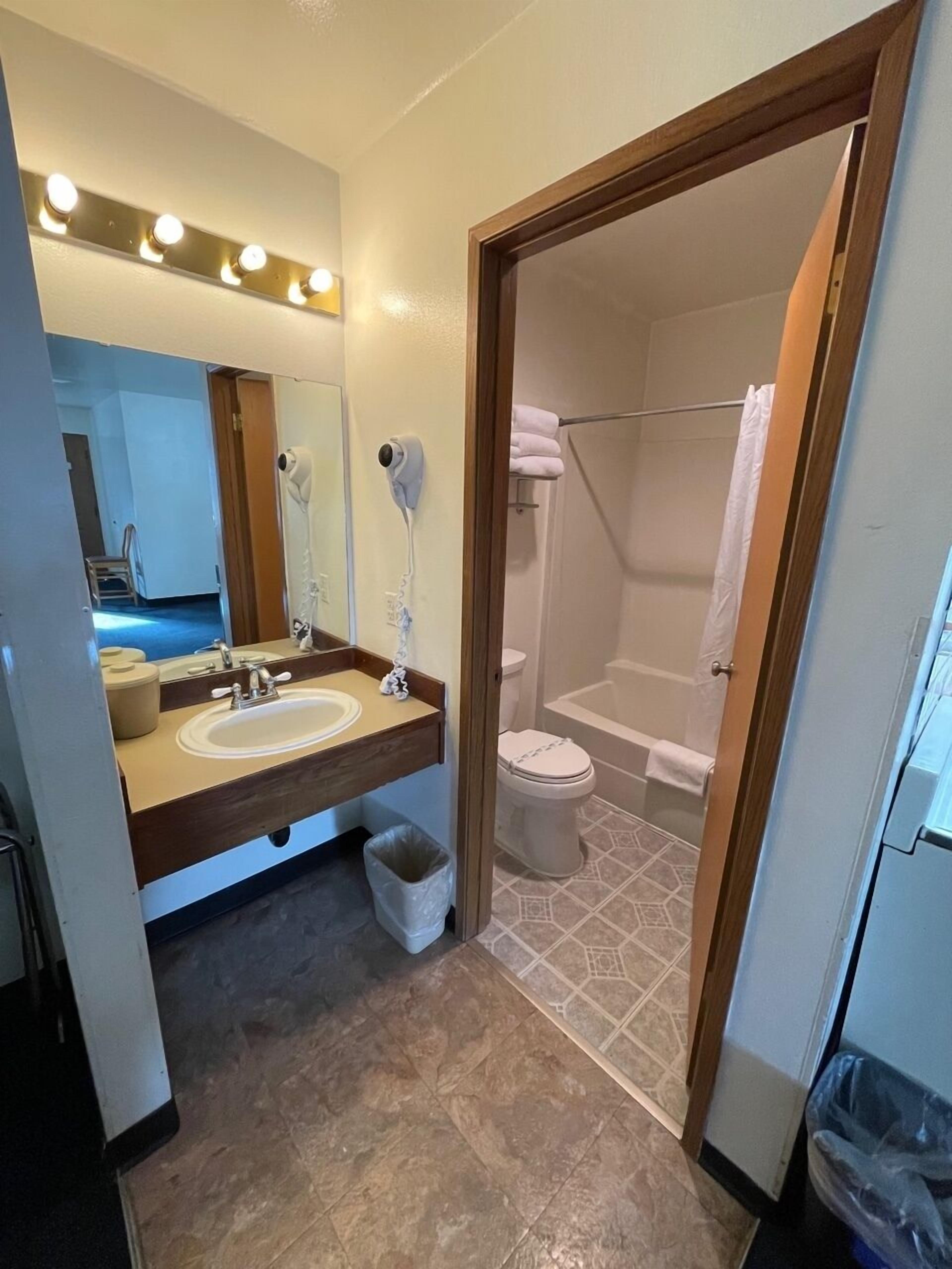 A bathroom with a sink, mirror, hairdryer, and a shower area.
