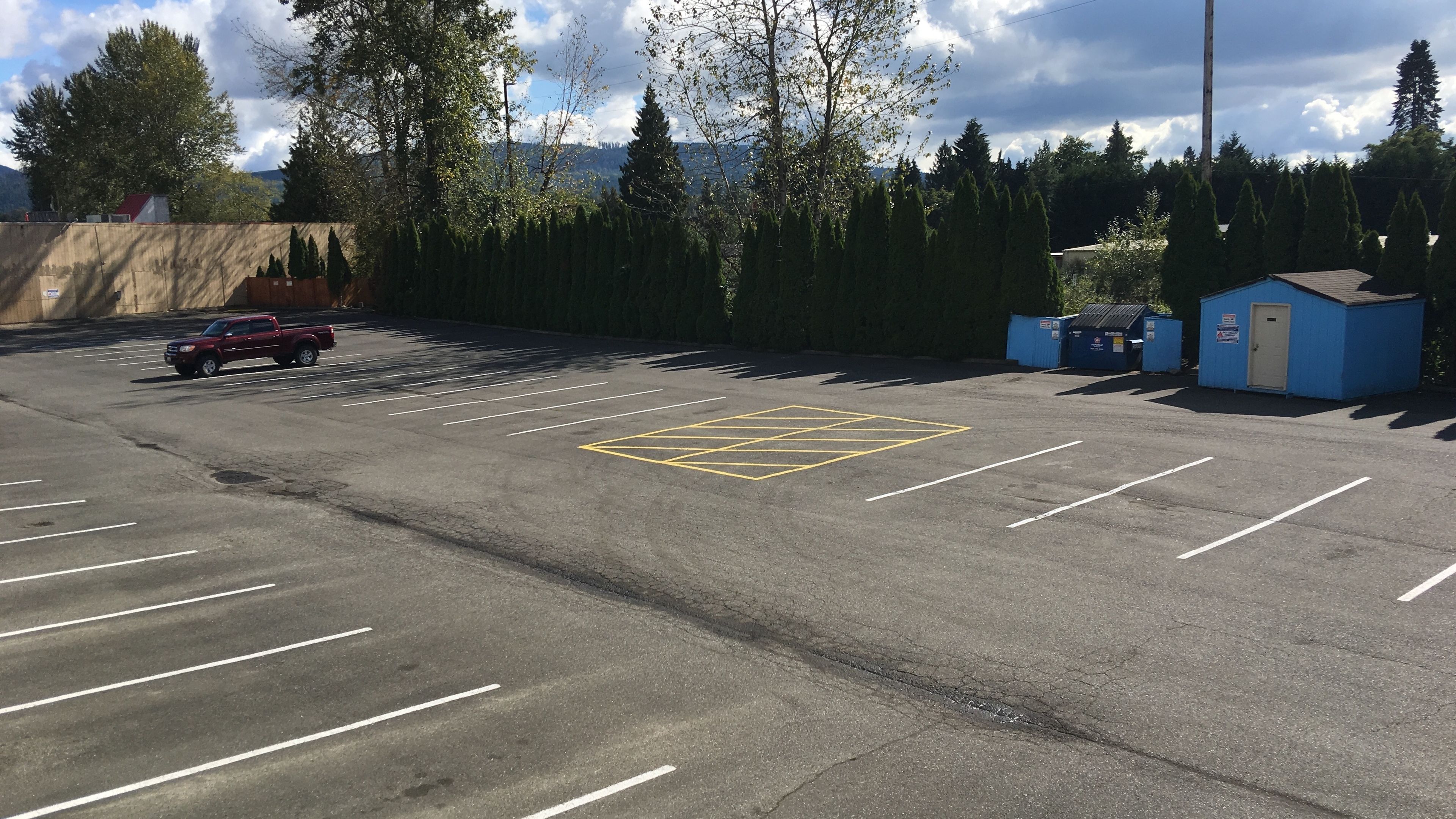 A parking lot with marked spaces, a red vehicle, and a small blue building.