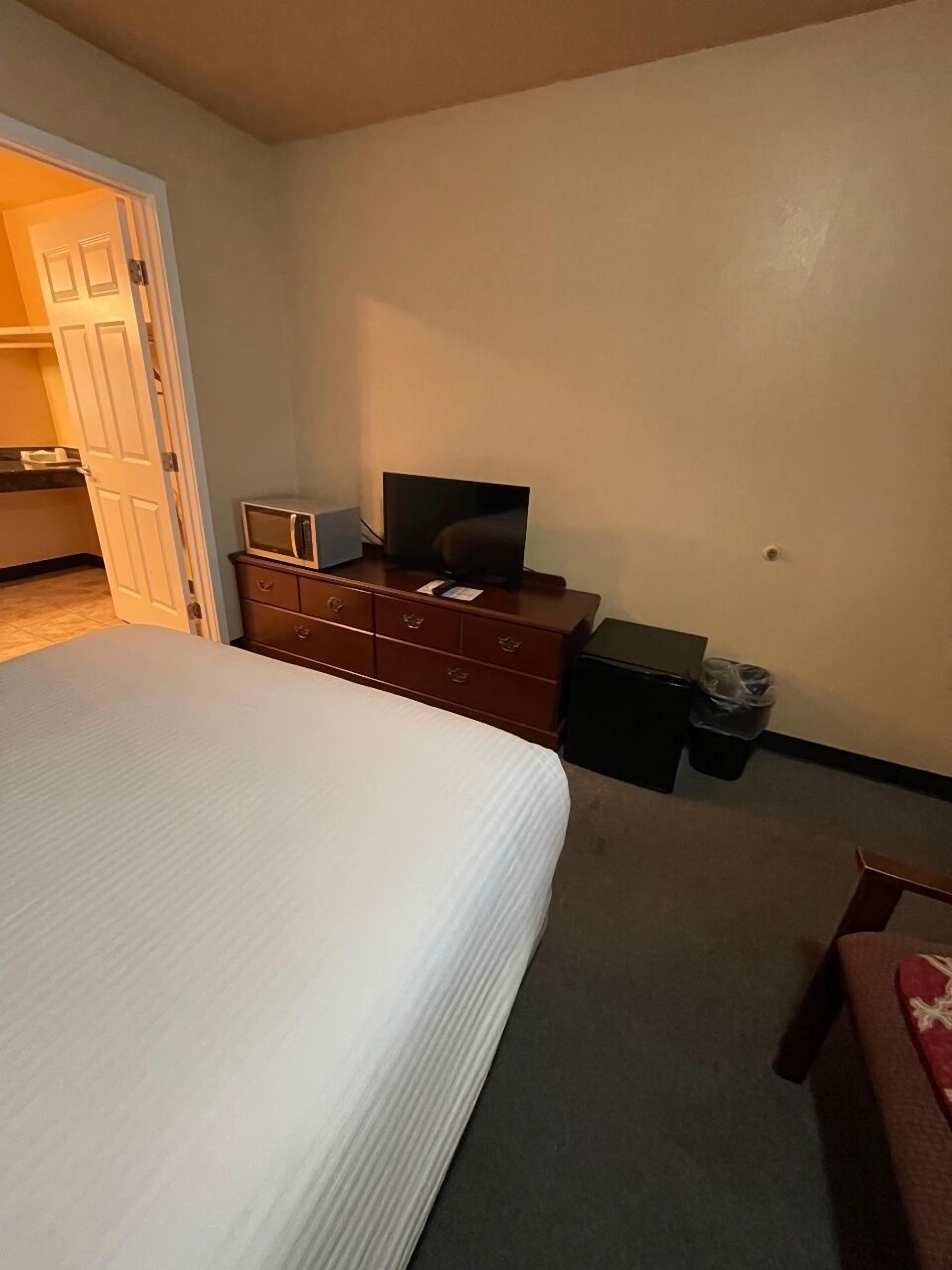A hotel room with a bed, a dresser, a television, and a trash bin.