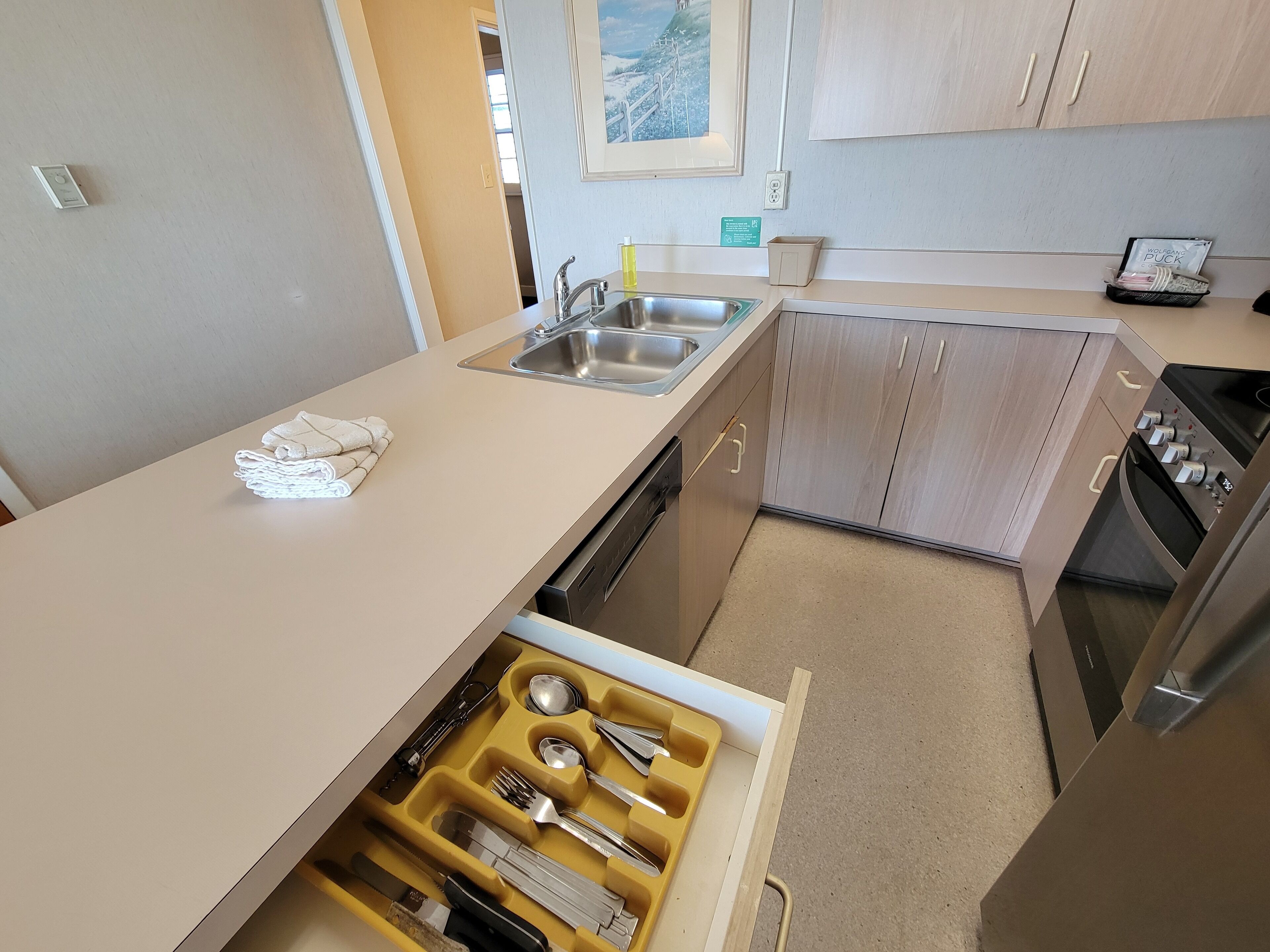 Cocina compacta con lavamanos, lavavajillas y un organizador de cajones con utensilios.