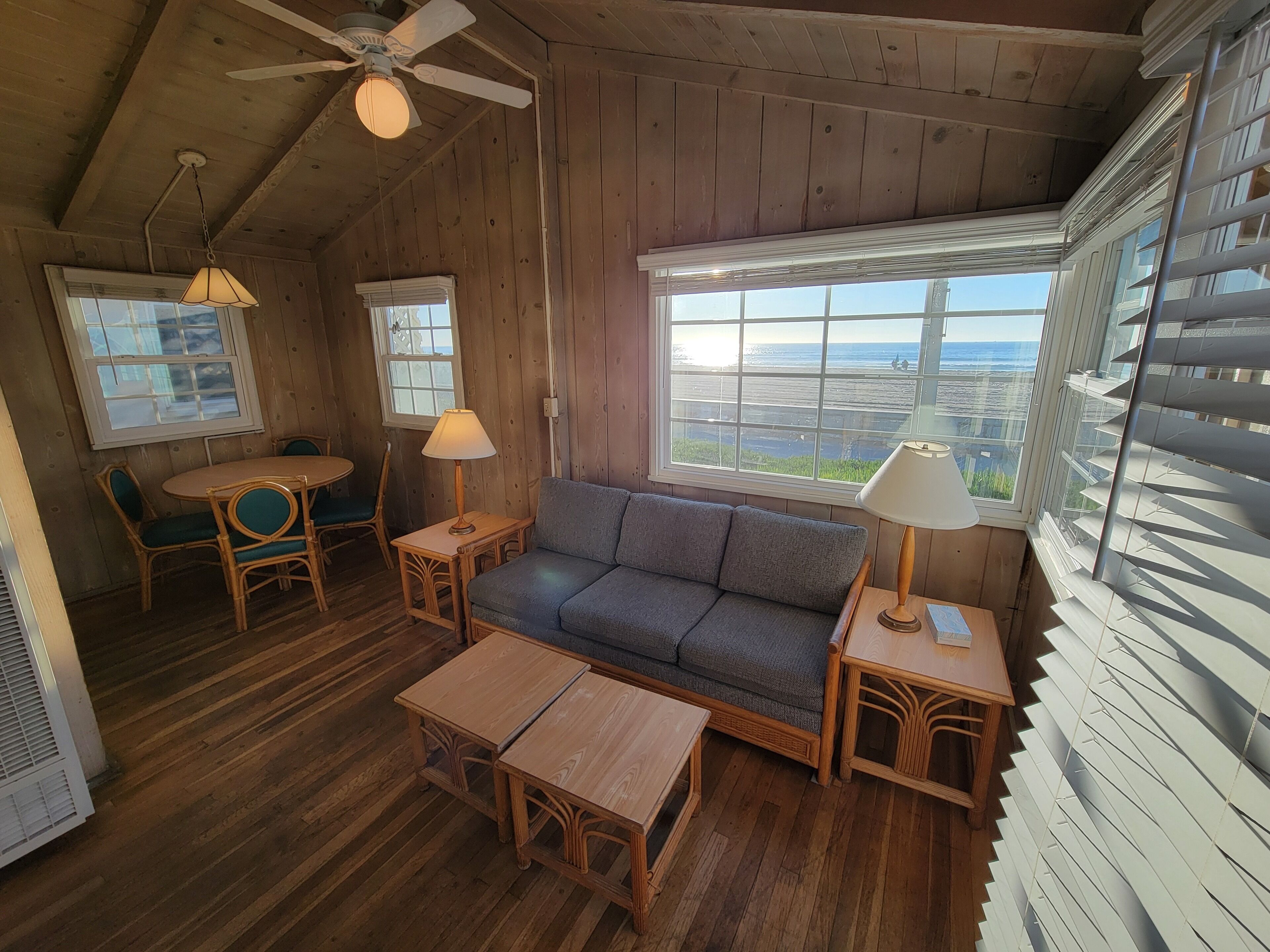 Ein gemütliches Blockhaus-Interieur mit Holzboden, einer Couch, einem Tisch, Stühlen und einem großen Fenster mit Blick auf den Strand.