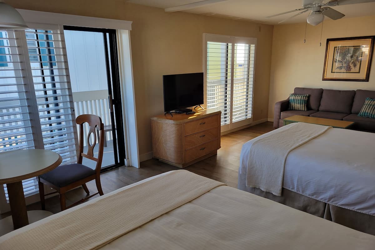 Ett hotellrum med två sängar, en tv på en byrå i trä, ett matbord med en stol och en soffa.