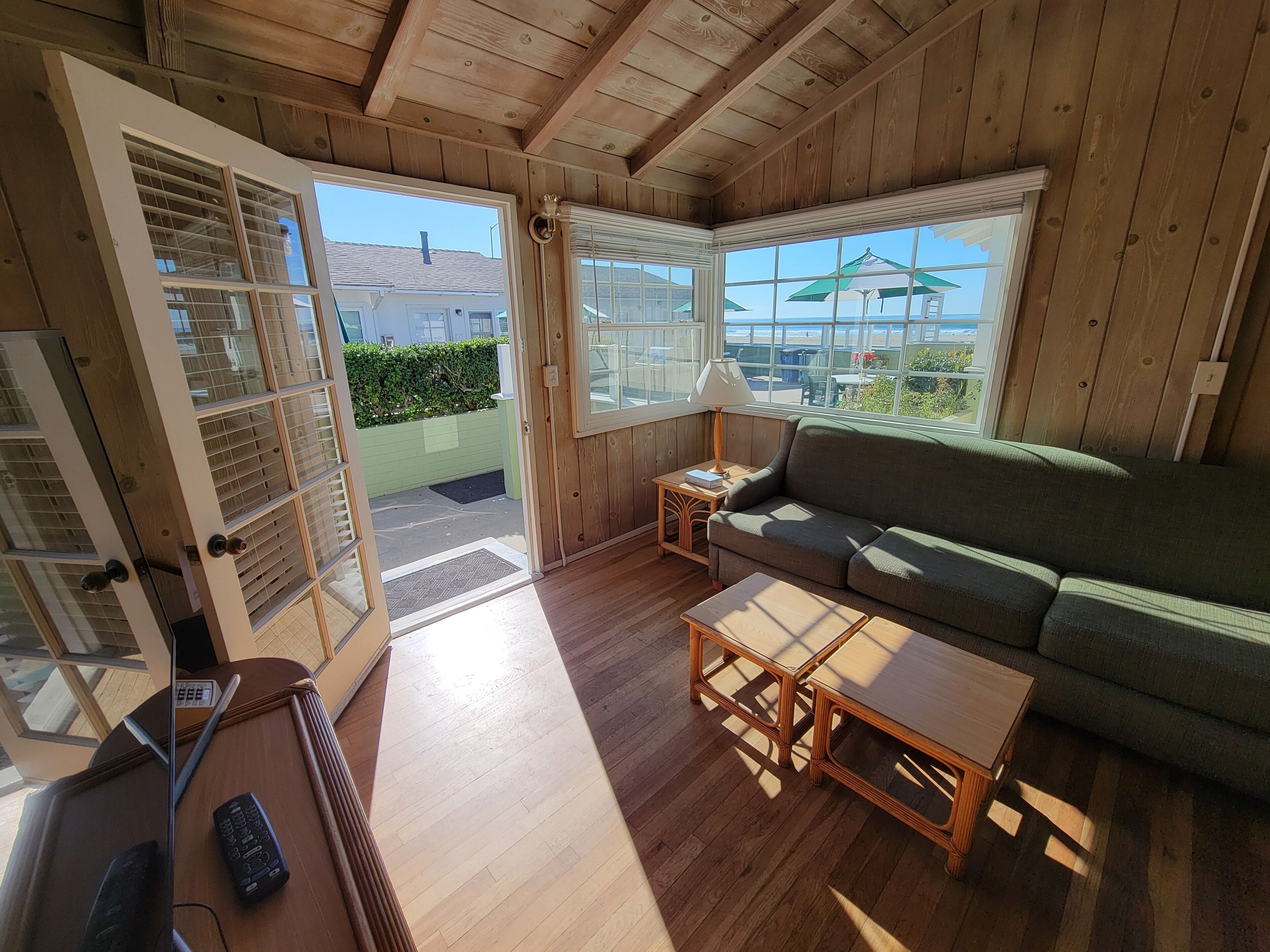 Un cuarto acogedor con techo de madera, un sofá verde, una mesita de centro de madera y una ventana con vistas a un jardín y un edificio.