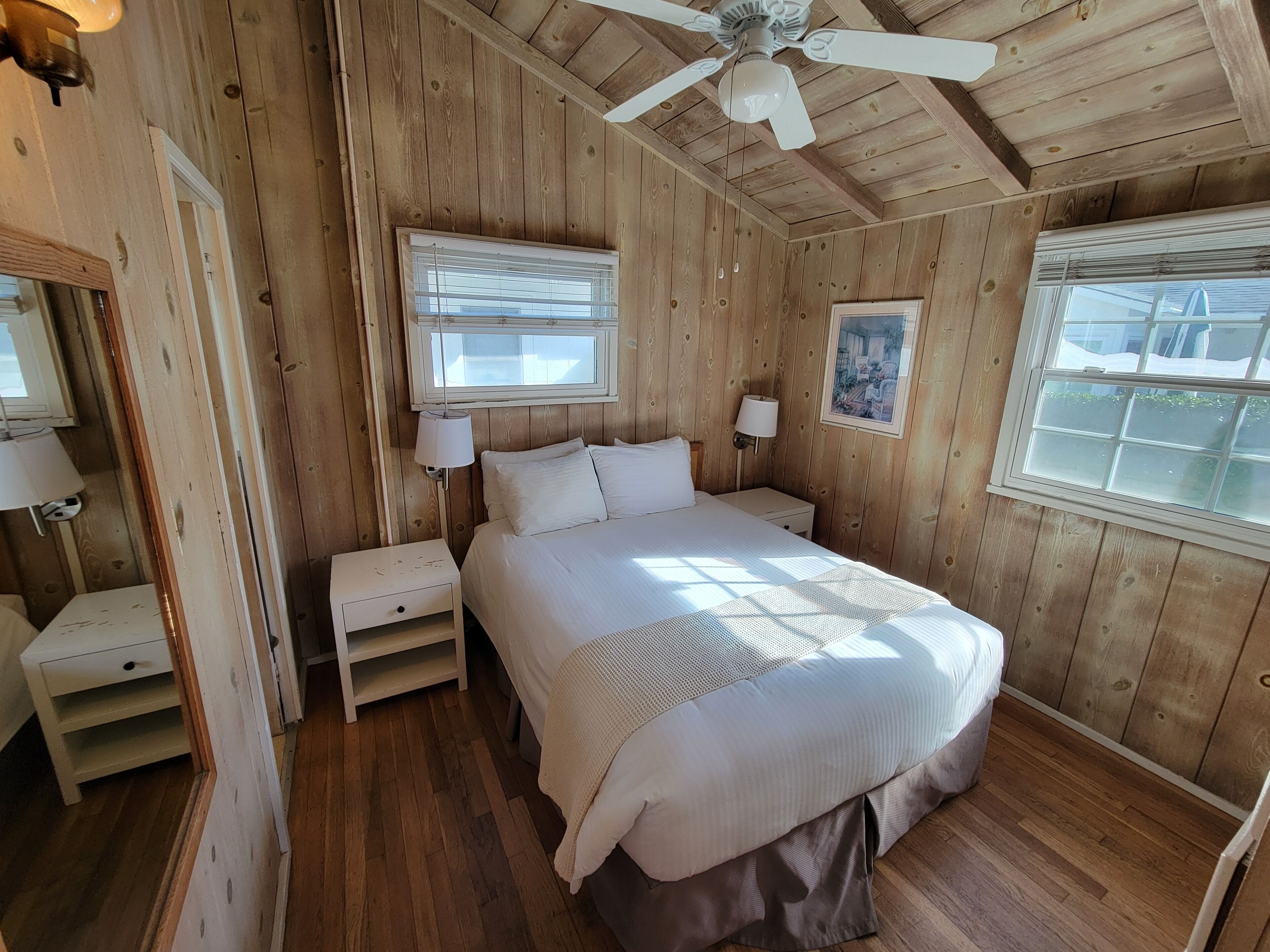 A wooden room with a bed, nightstands, and a ceiling fan.