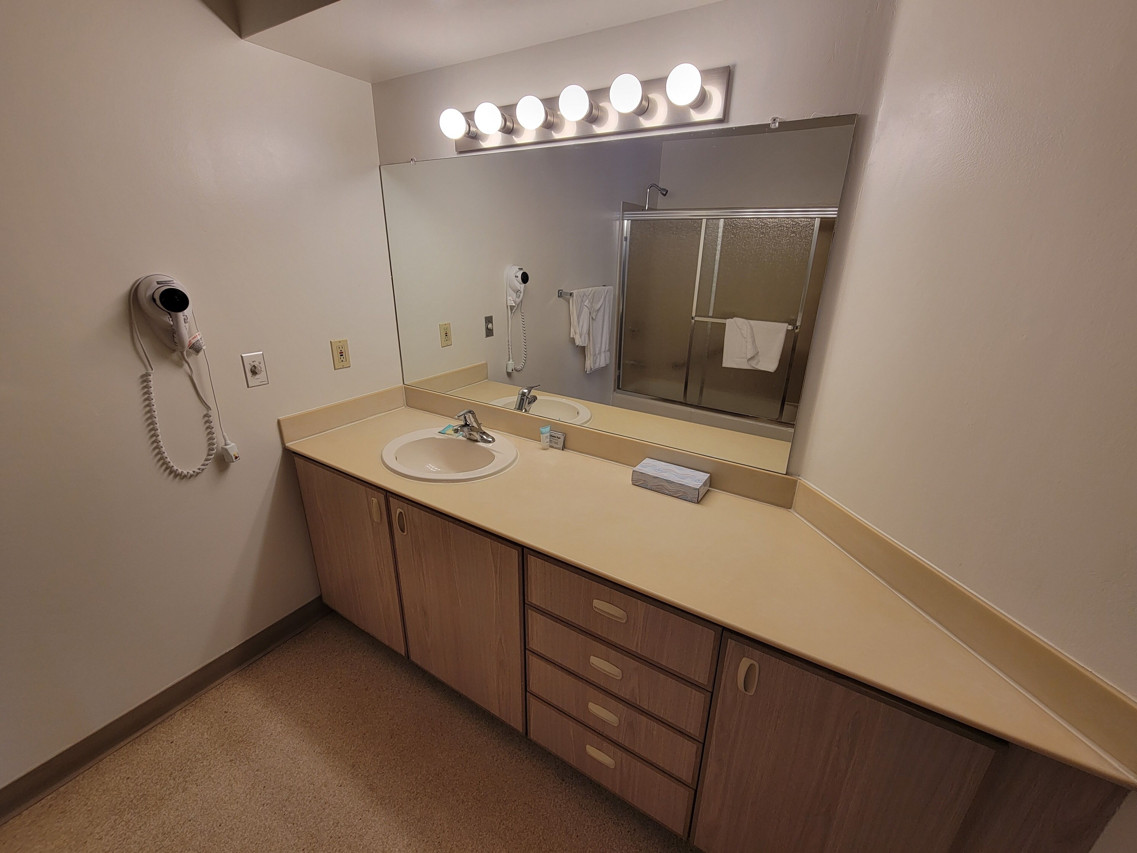 A bathroom with a sink, mirror, vanity, and a hairdryer on the wall.