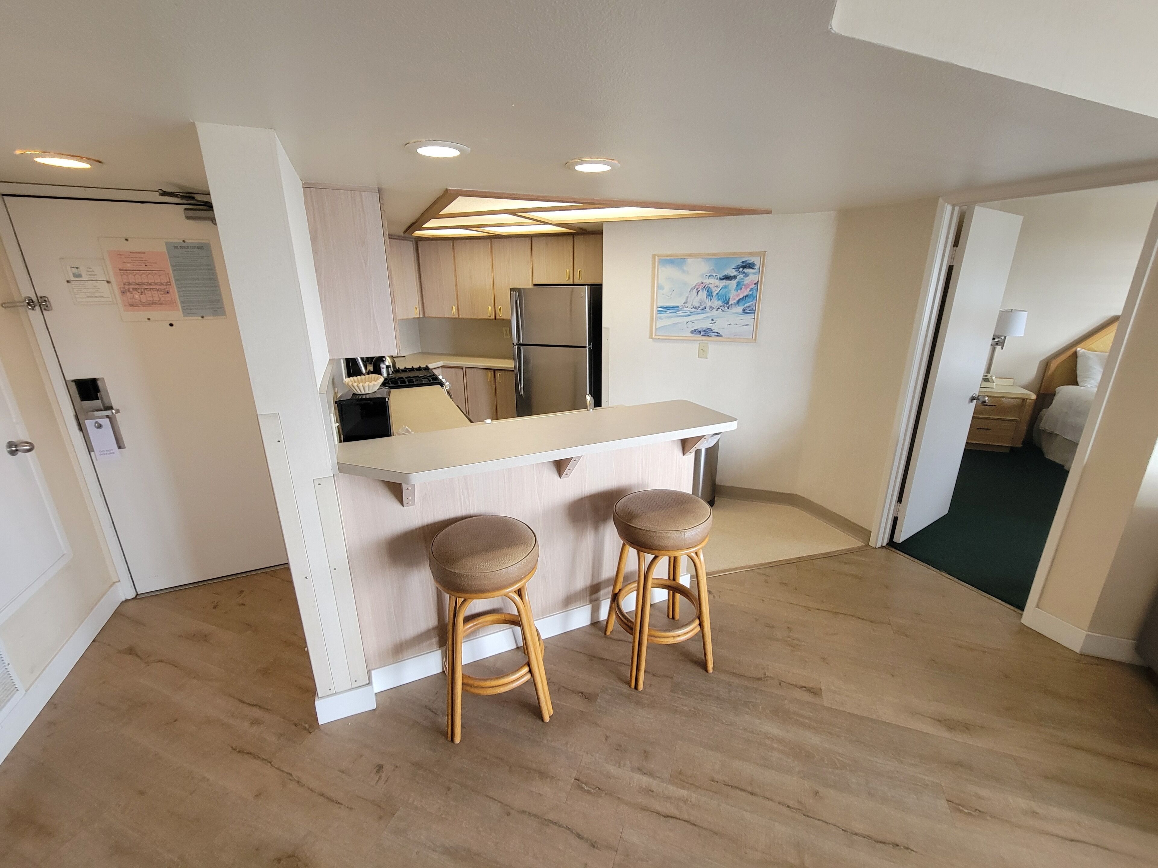 A compact kitchen with a central island, two stools, and a refrigerator.