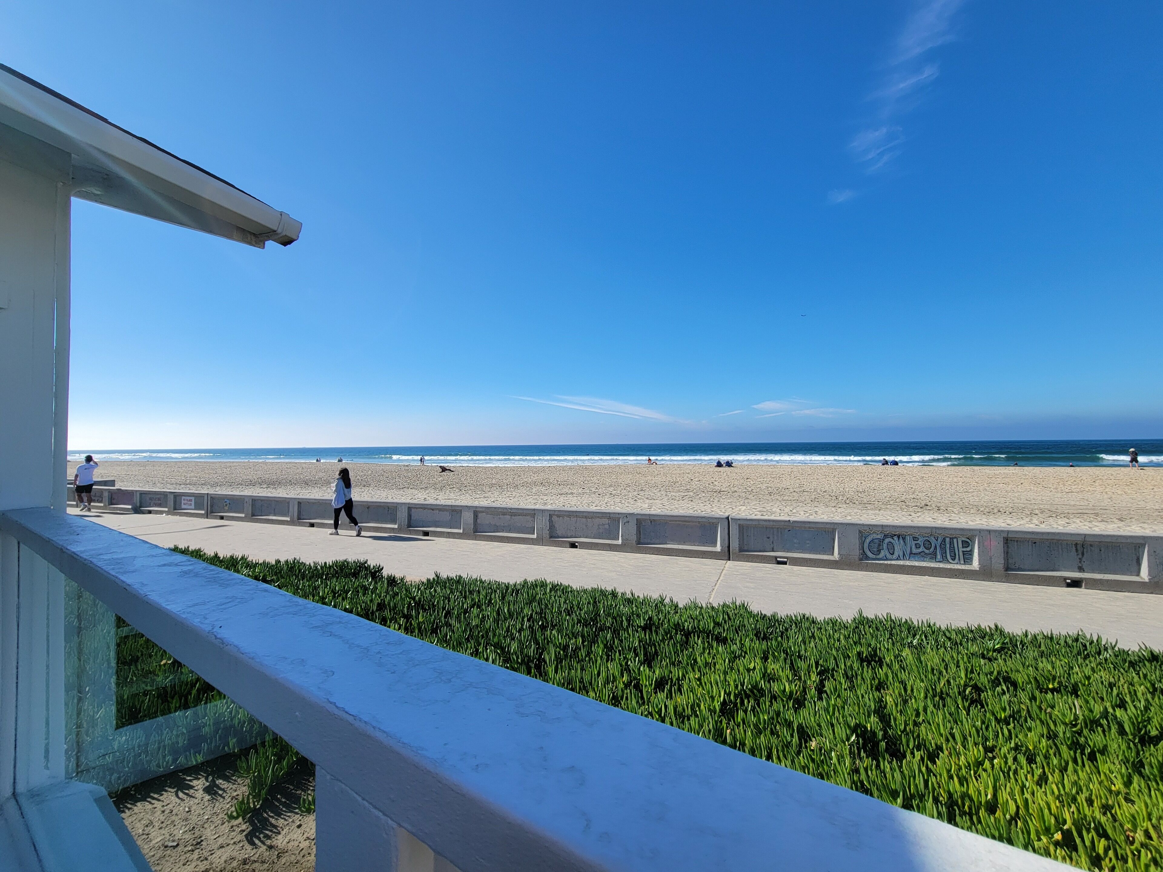 A beach with a concrete walkway and a grassy area in the foreground.