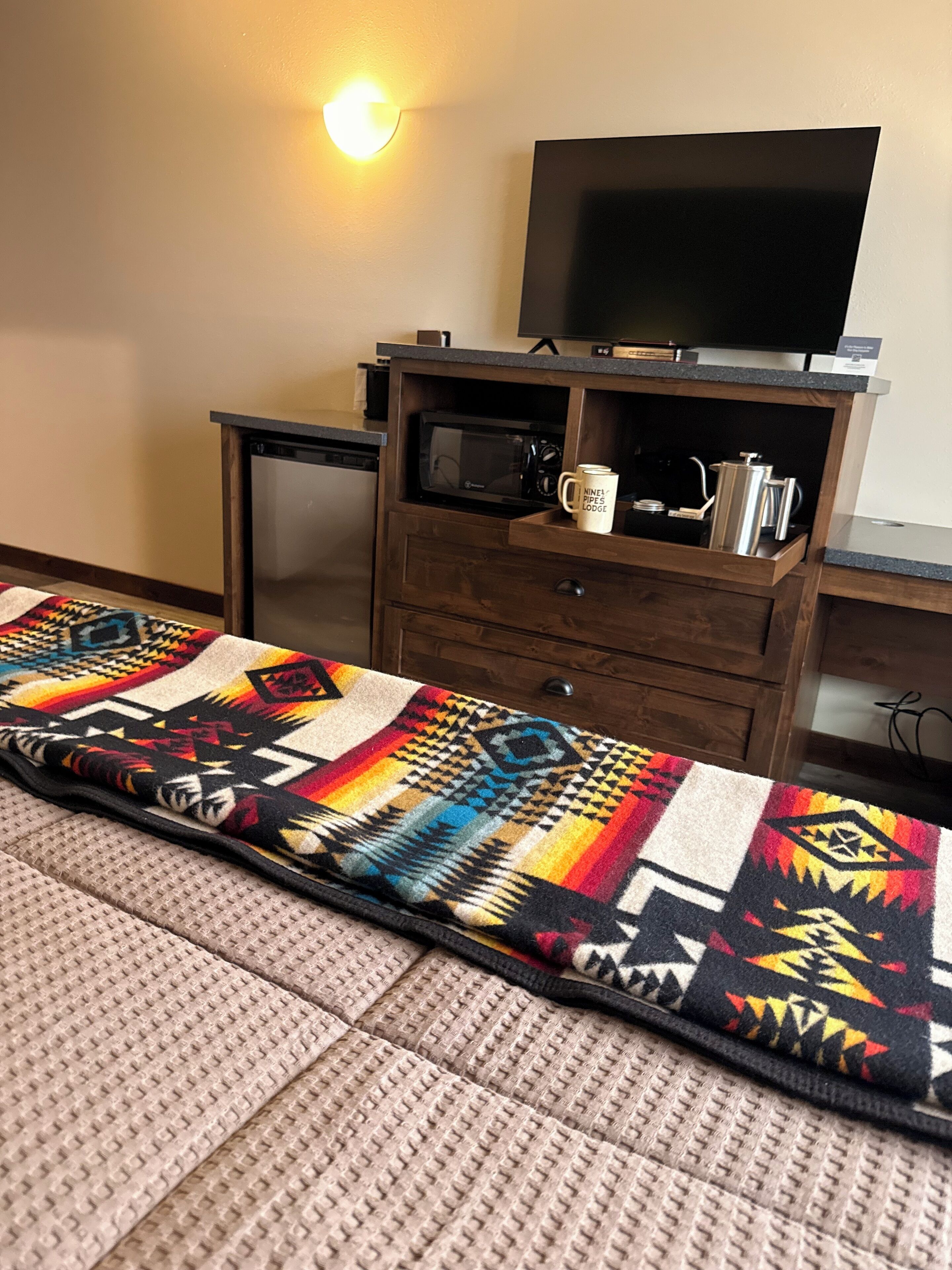 A room with a microwave, a coffee mug, a television, and a colorful blanket on the floor.