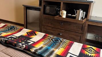 A room with a microwave, a coffee mug, a television, and a colorful blanket on the floor.