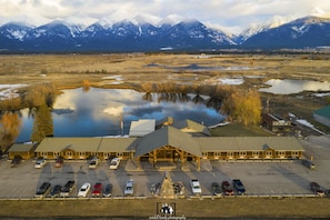 A lodge with a large parking lot, a pond, and mountains in the background.