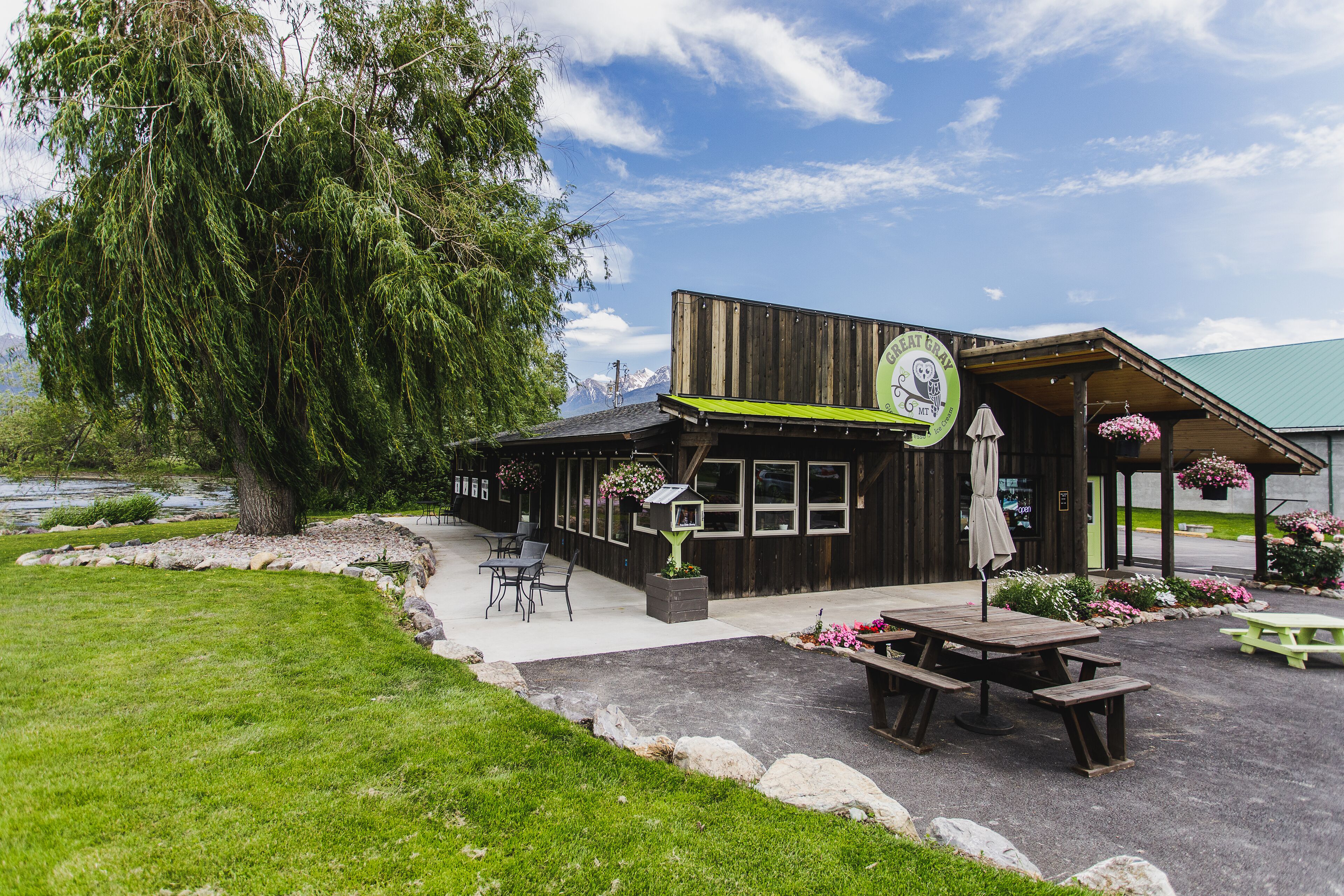 A rustic building with a green awning, outdoor seating, and a large tree in the background.
