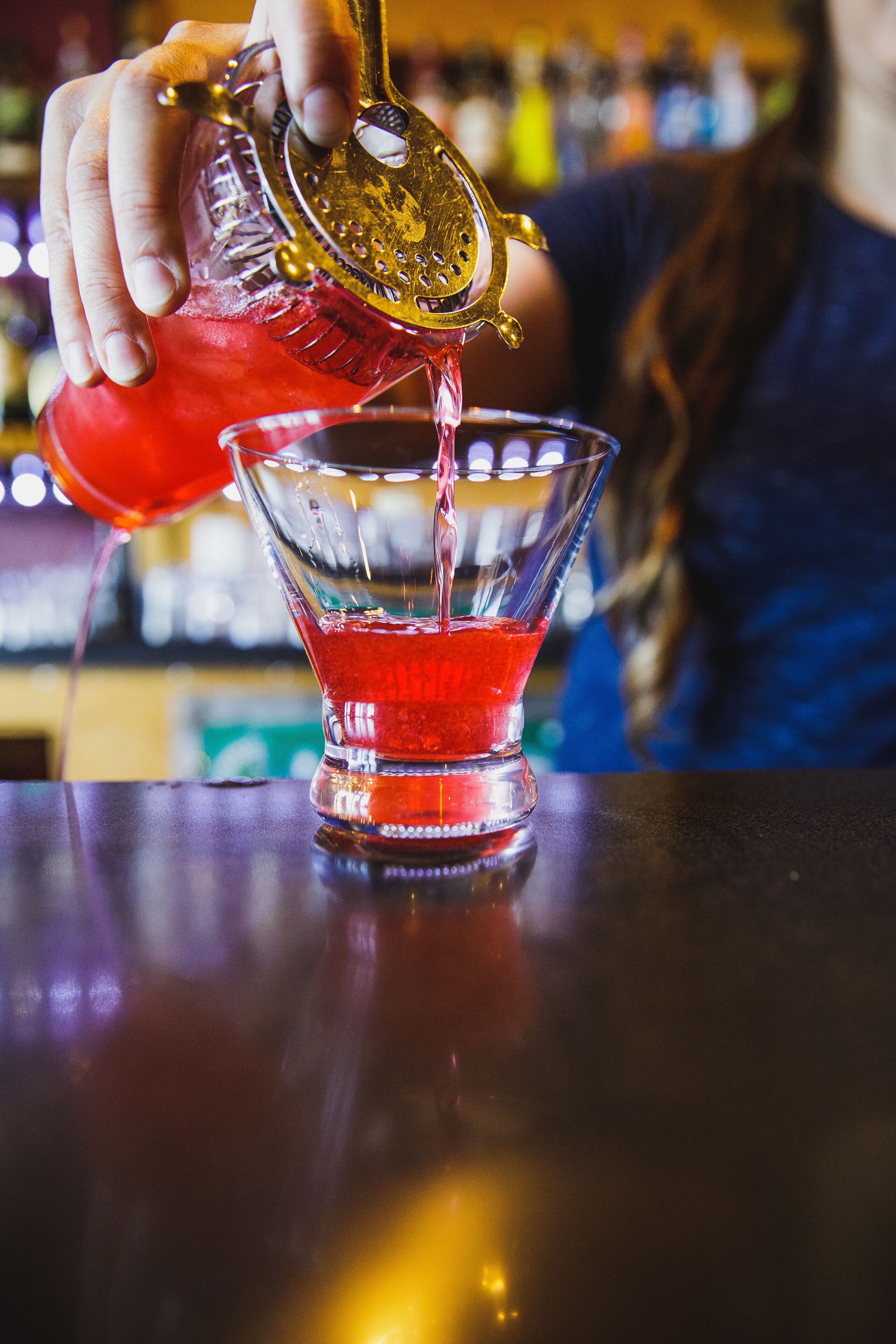 A hand pouring a red liquid into a clear glass with a stem.