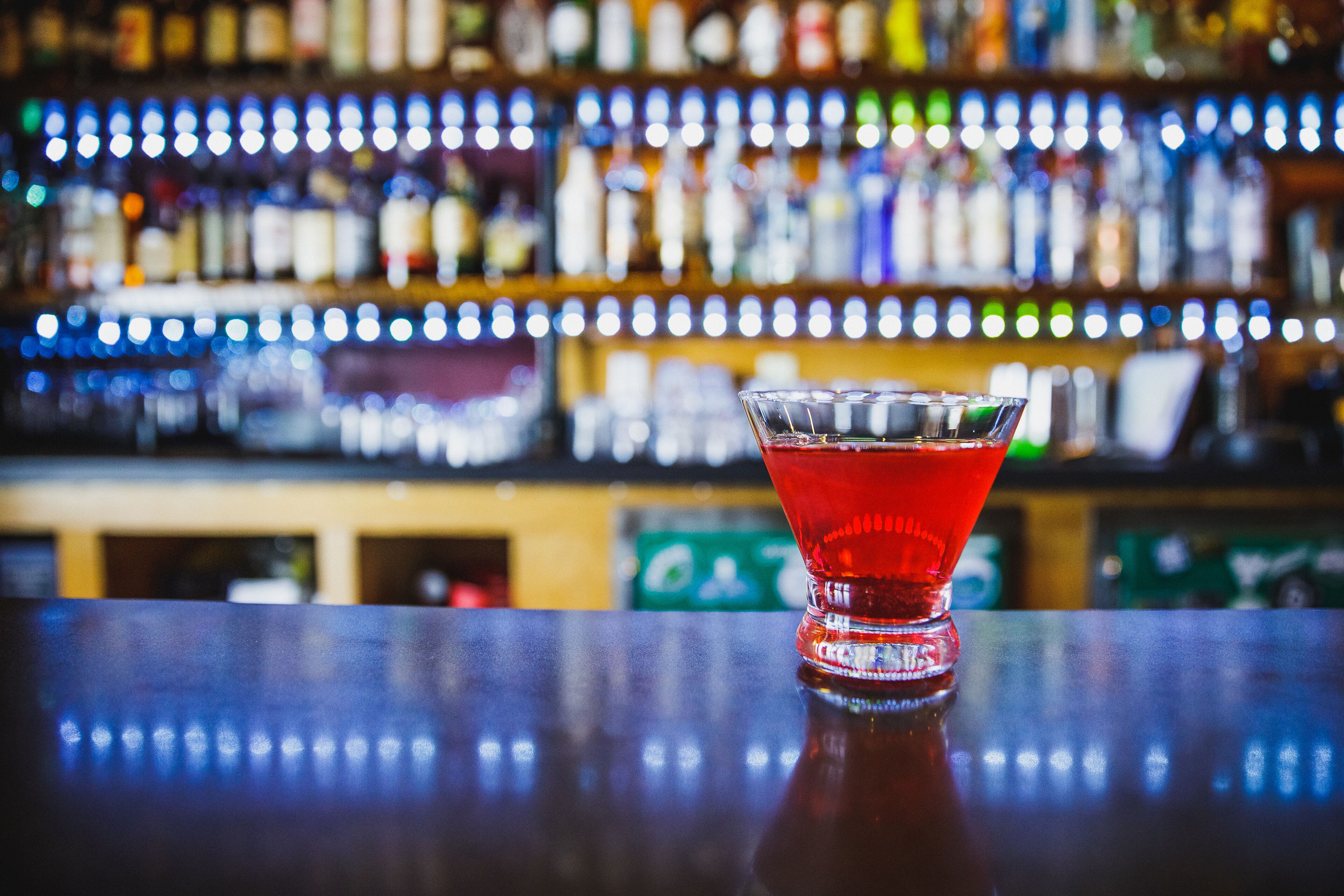 A bar with a glass of red cocktail on the counter.