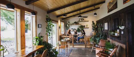 A rustic interior with wooden beams, large windows, and indoor plants.