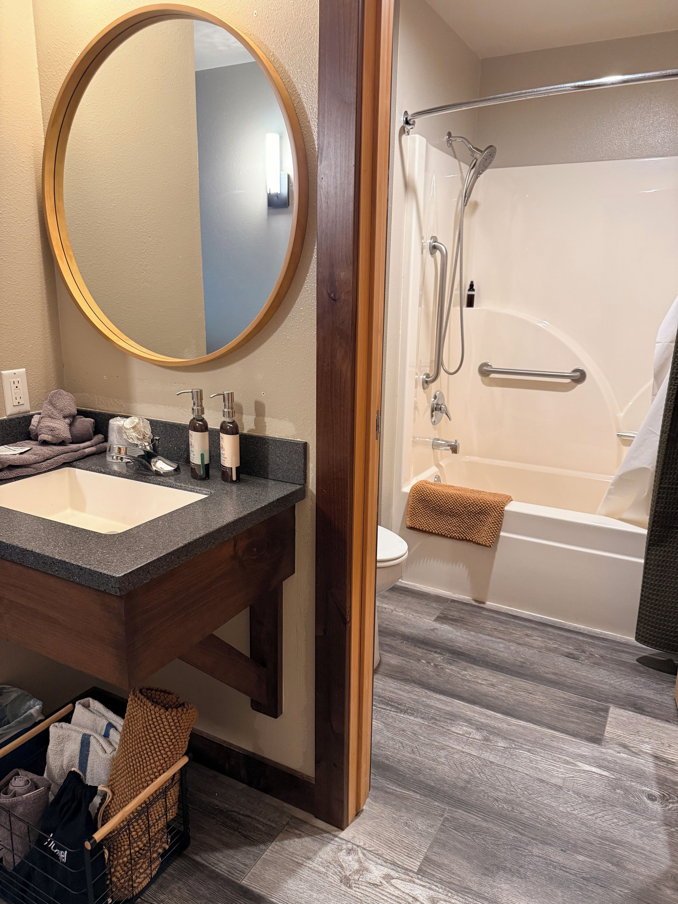 A bathroom with a wooden vanity, a round mirror, a bathtub, and a shower.