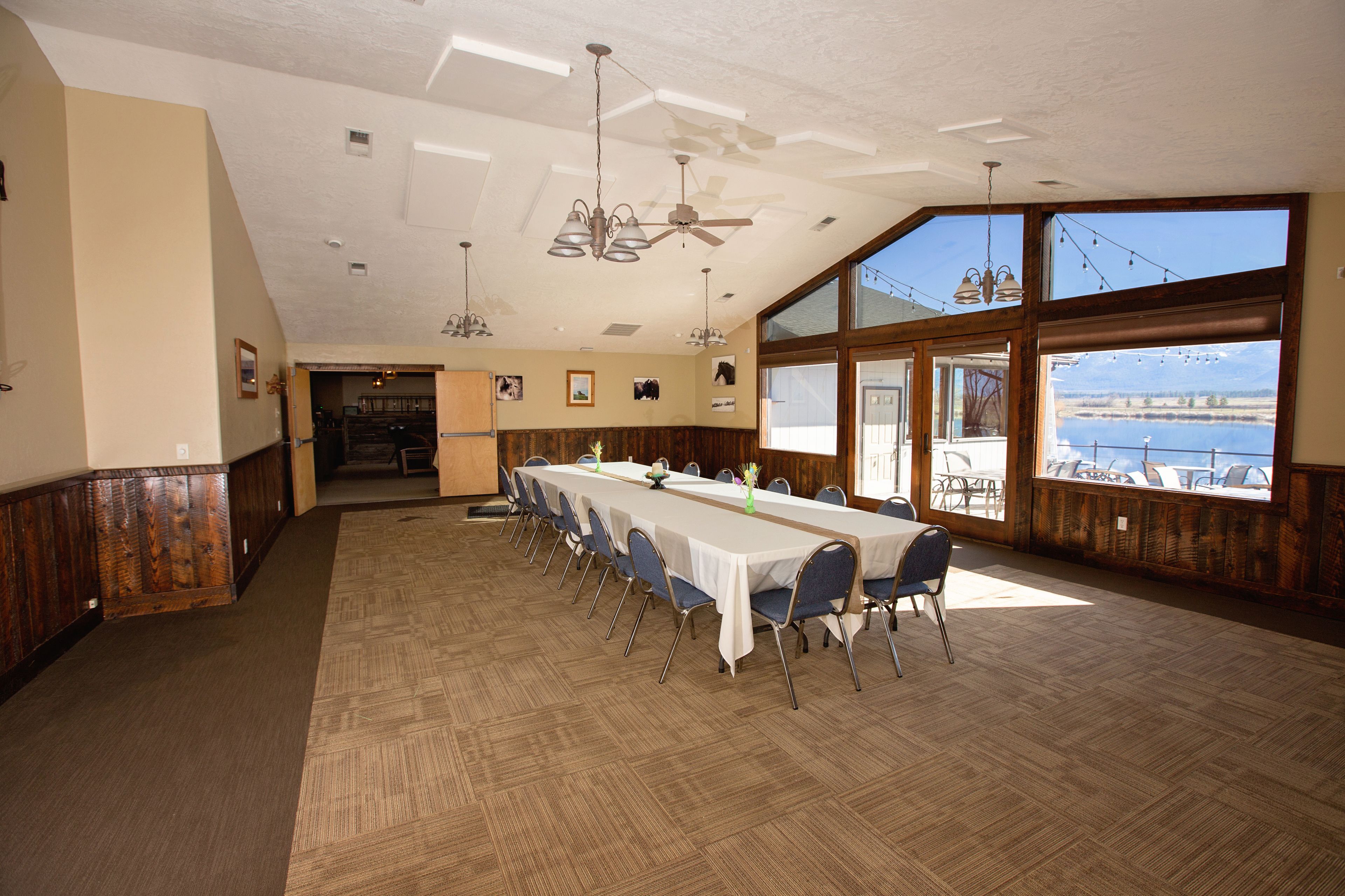 Une grande salle de conférence dotée d’une longue table, de chaises, de ventilateurs de plafond et de grandes fenêtres offrant une vue sur une étendue d’eau.
