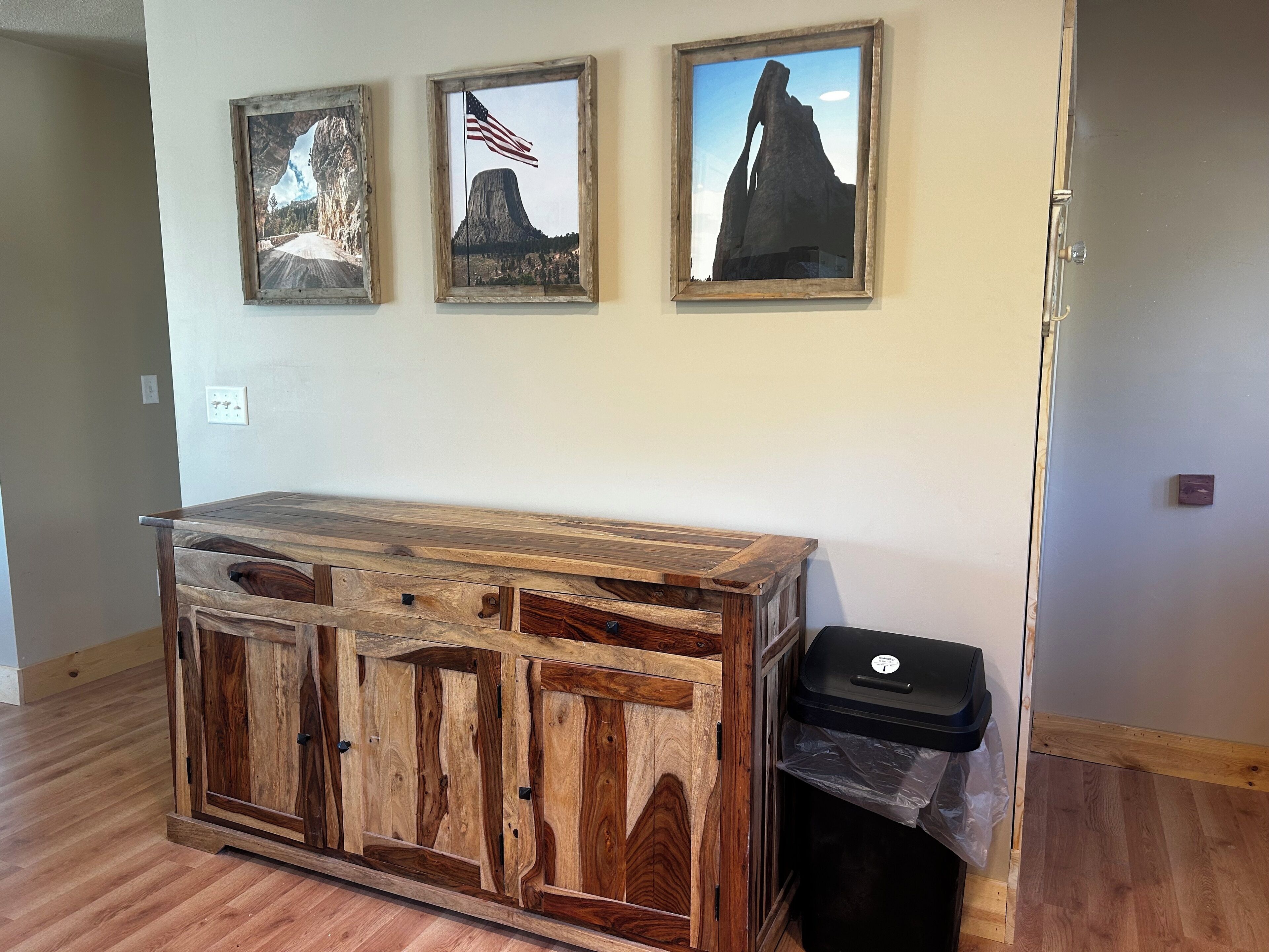 Un mueble de madera con cajones y un cubo de basura en una habitación con suelo de madera y pared blanca.