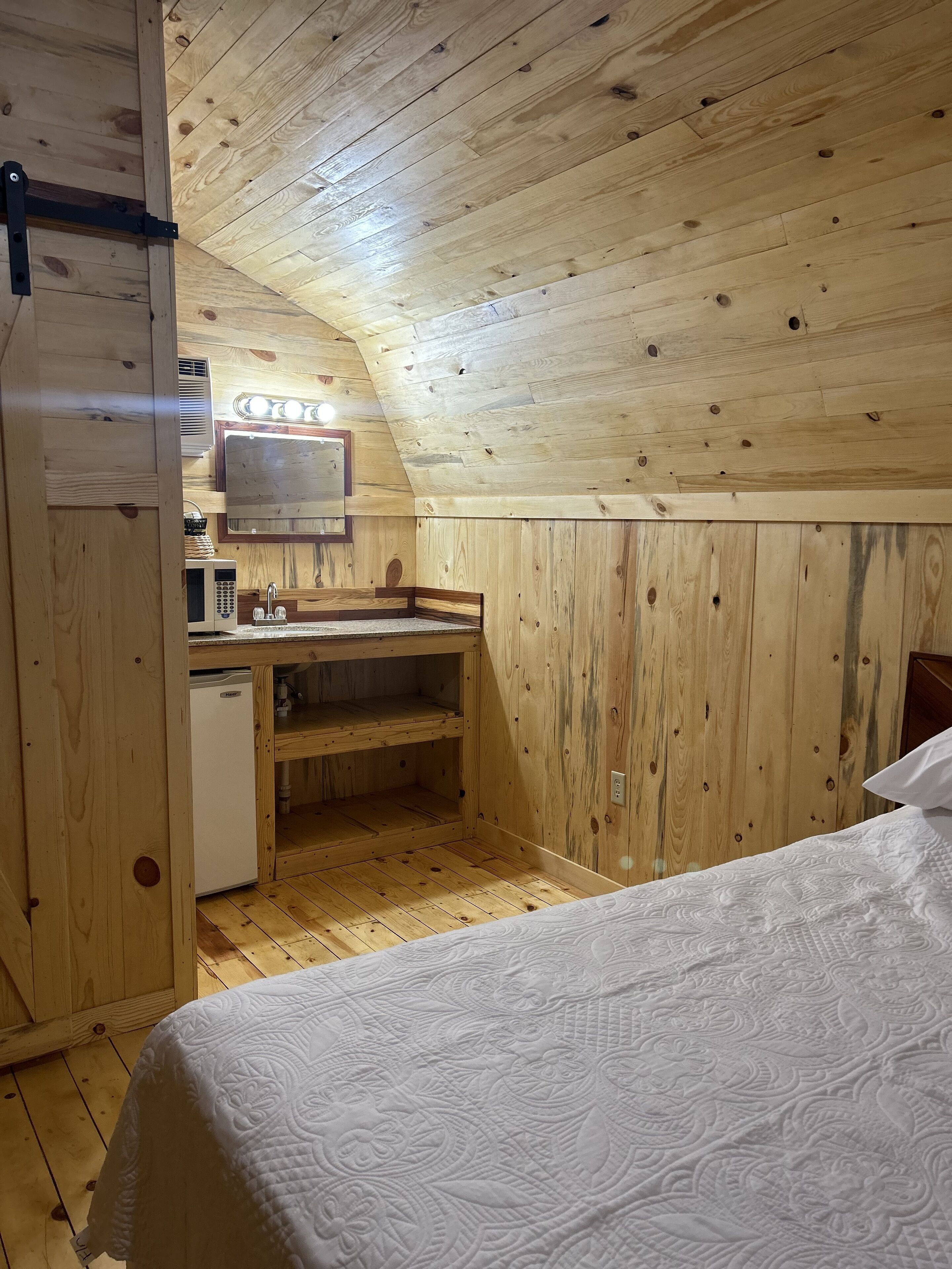 Une petite cabane en bois comprenant un coin cuisine, un lit et un plafond en pente.