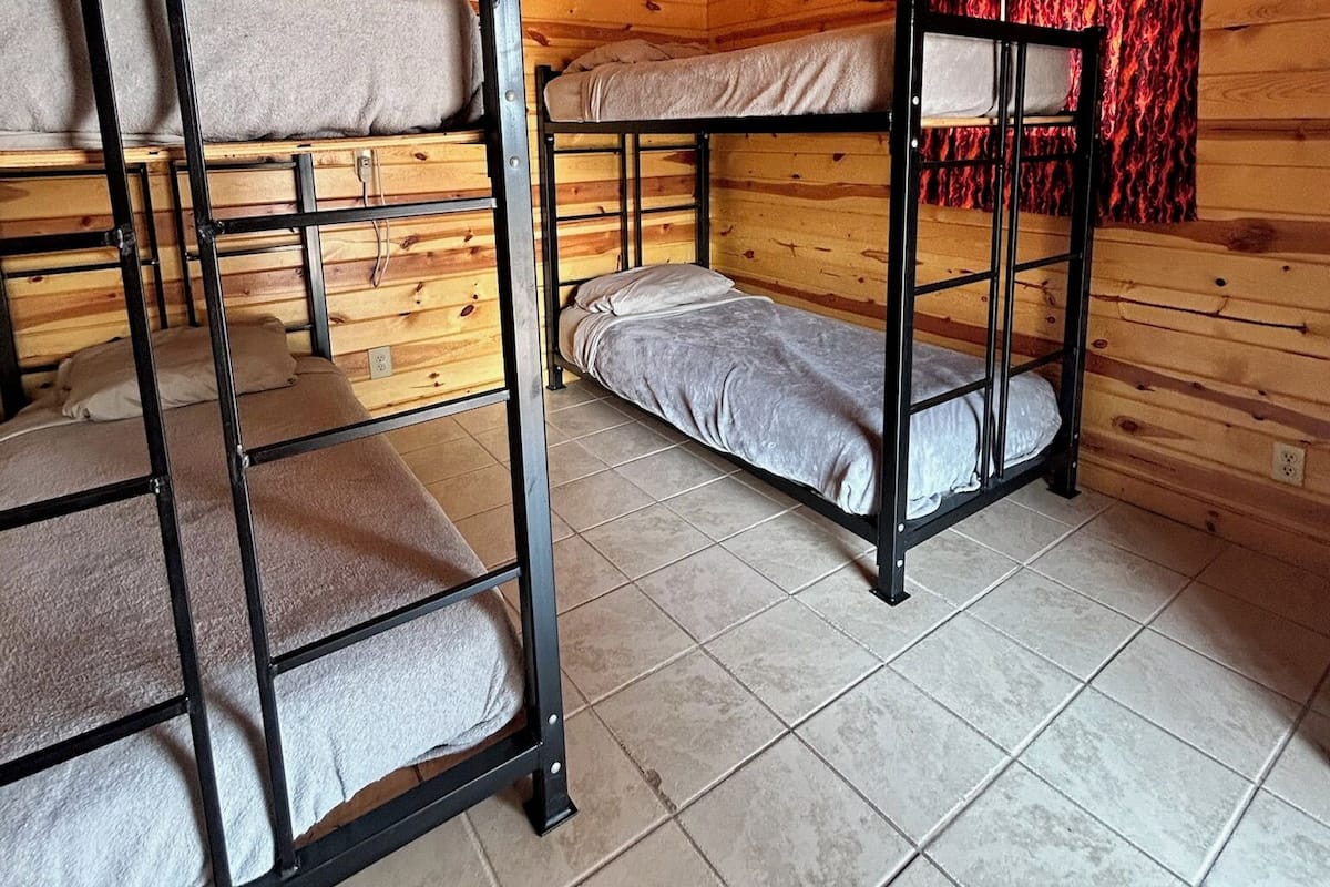 A cabin with bunk beds, wooden walls, a ceiling fan, and a red curtain.