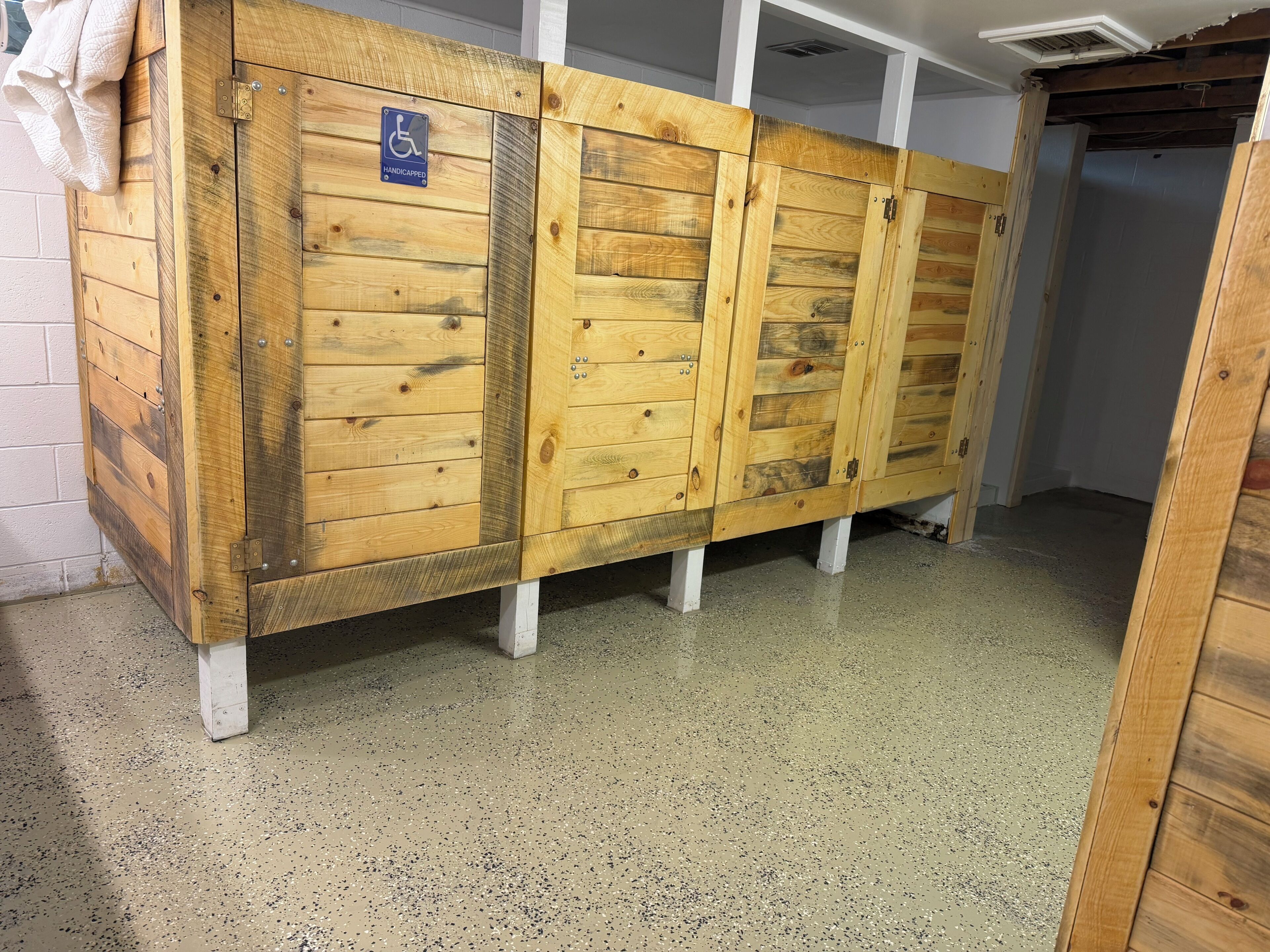 A wooden locker room with a handicap sign, white pillars, and a speckled floor.