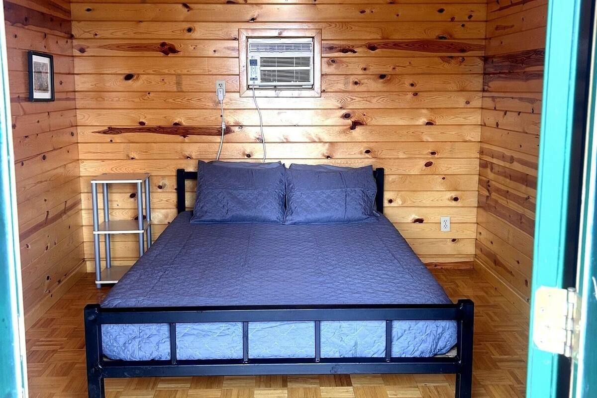 A wooden cabin bedroom with a bed, a ceiling fan, and an air conditioning unit.