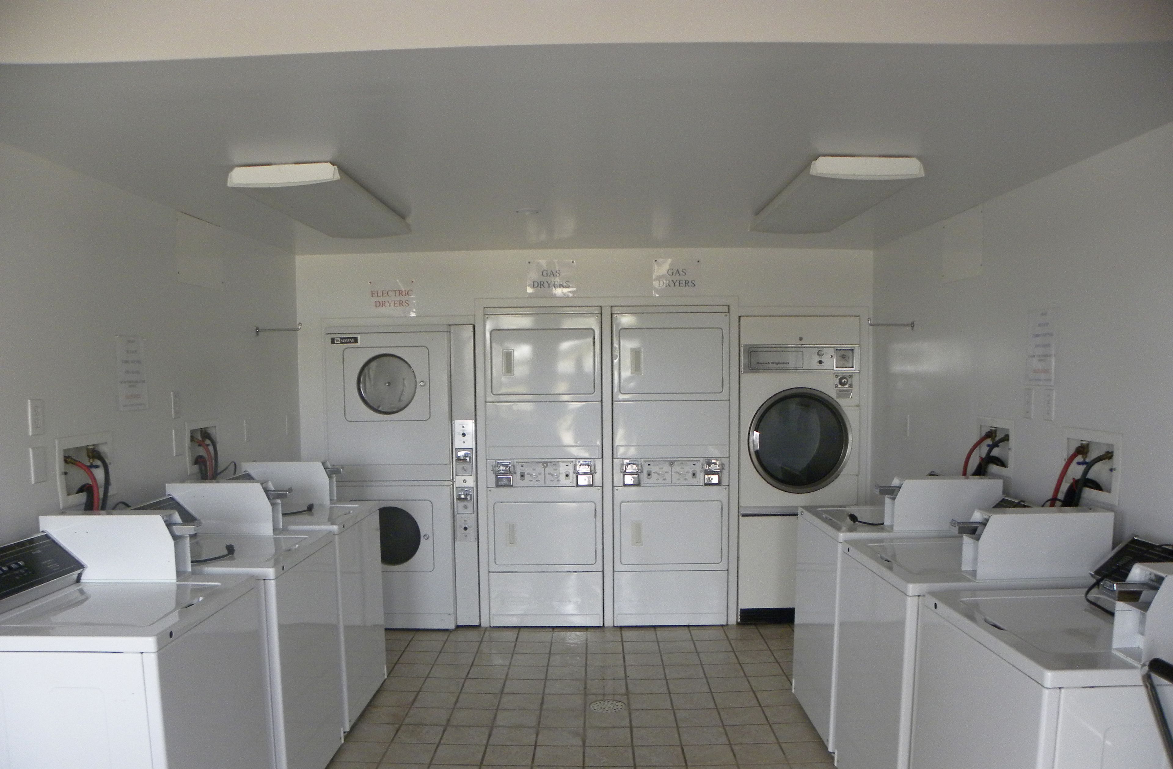 A laundry room with rows of washers and dryers, control panels, and electrical outlets.