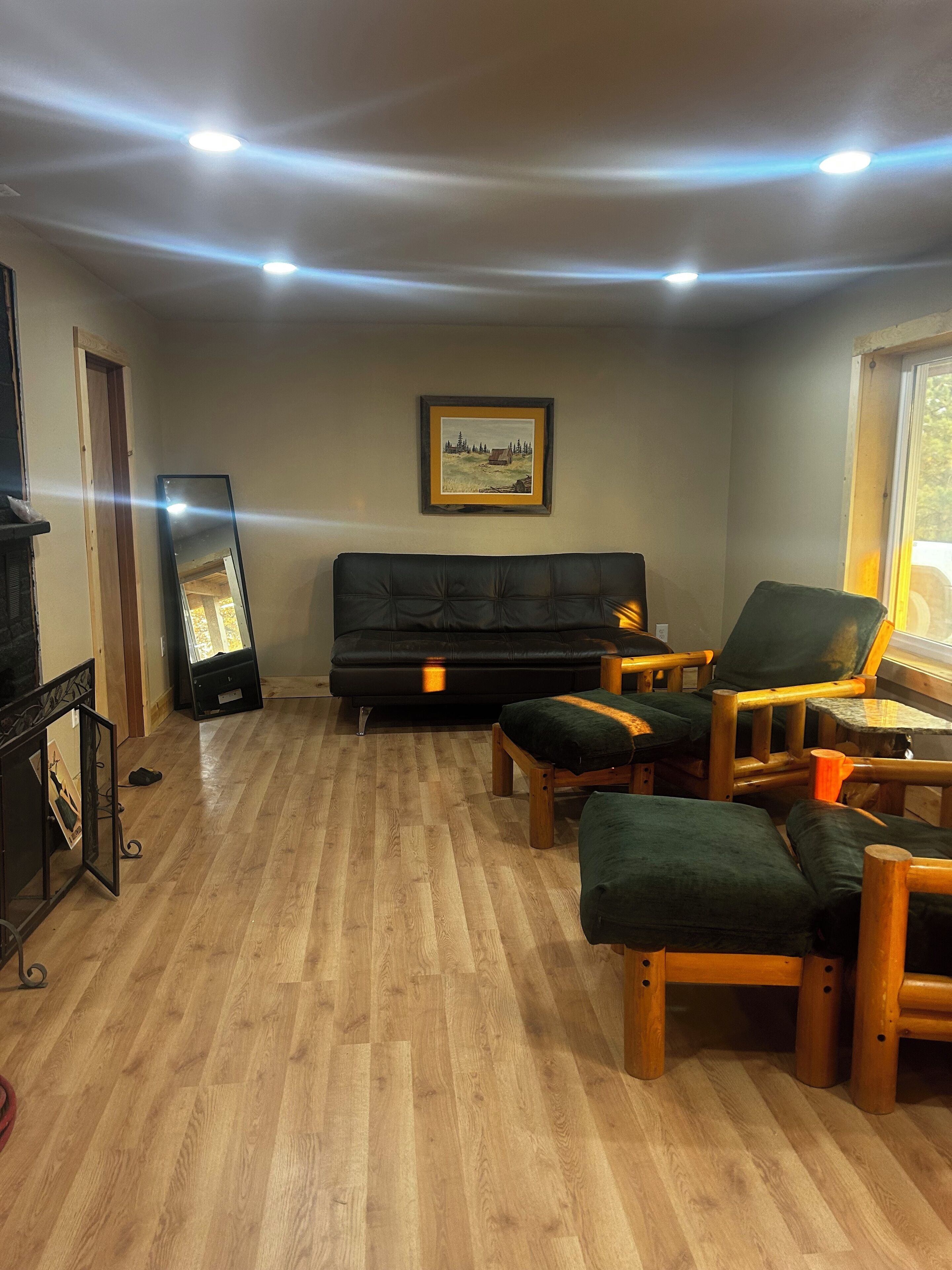A living room with a black leather sofa, wooden chairs, a framed picture on the wall, and a fireplace.