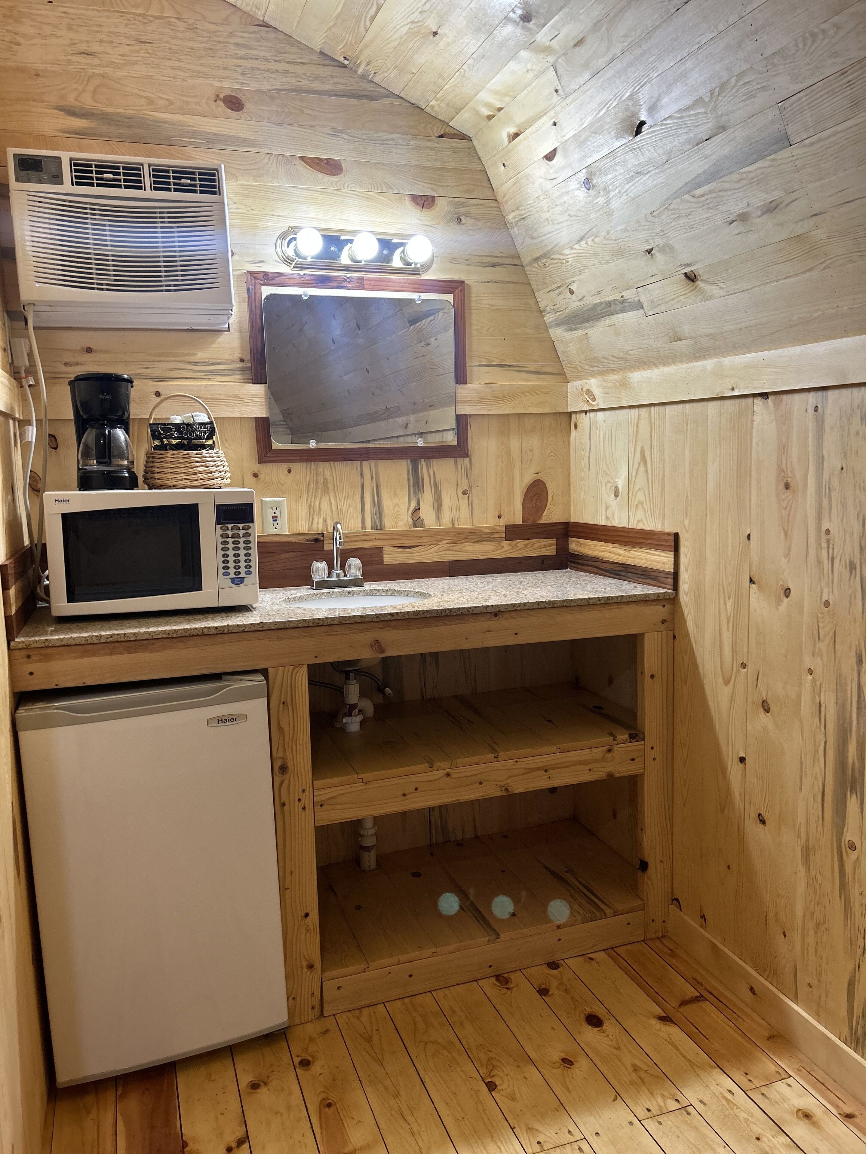 A compact kitchen with wooden walls, a microwave, a coffee maker, and a sink.
