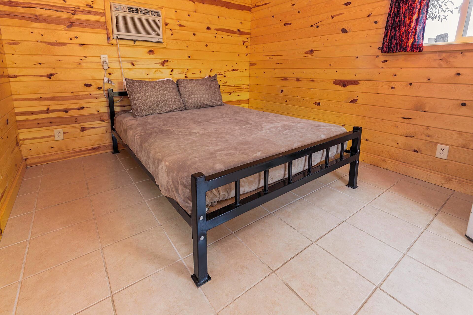 A wooden cabin room with a bed, a window, and a wall-mounted air conditioner.