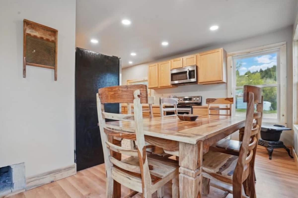 A modern kitchen with wooden cabinetry, a large dining table, and a view of the outdoors.