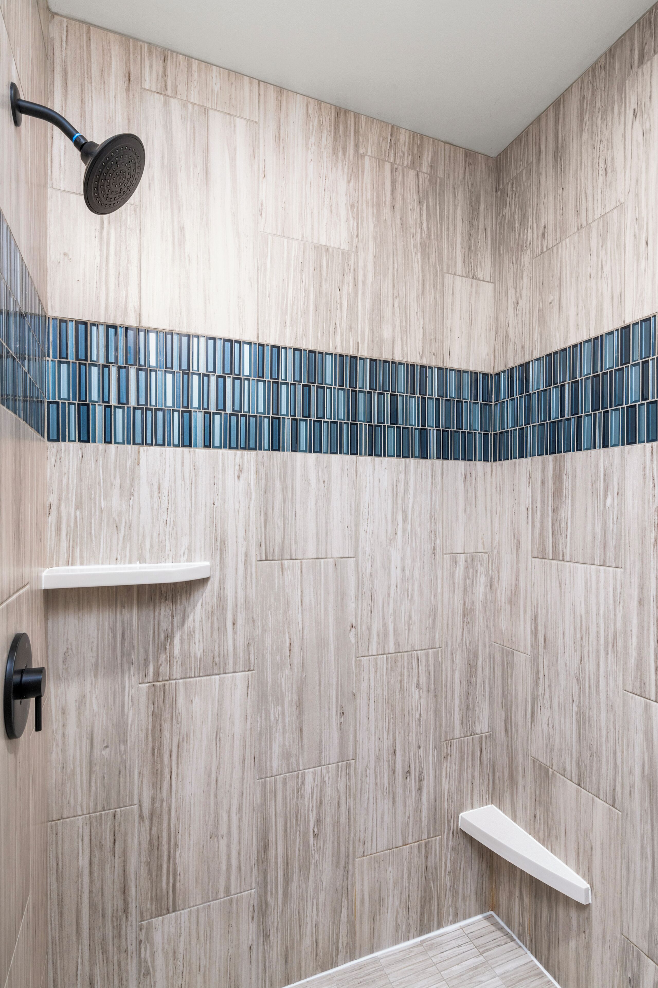 Een douchegedeelte met een houten wand, een blauw betegeld plankje en een witte plank.
