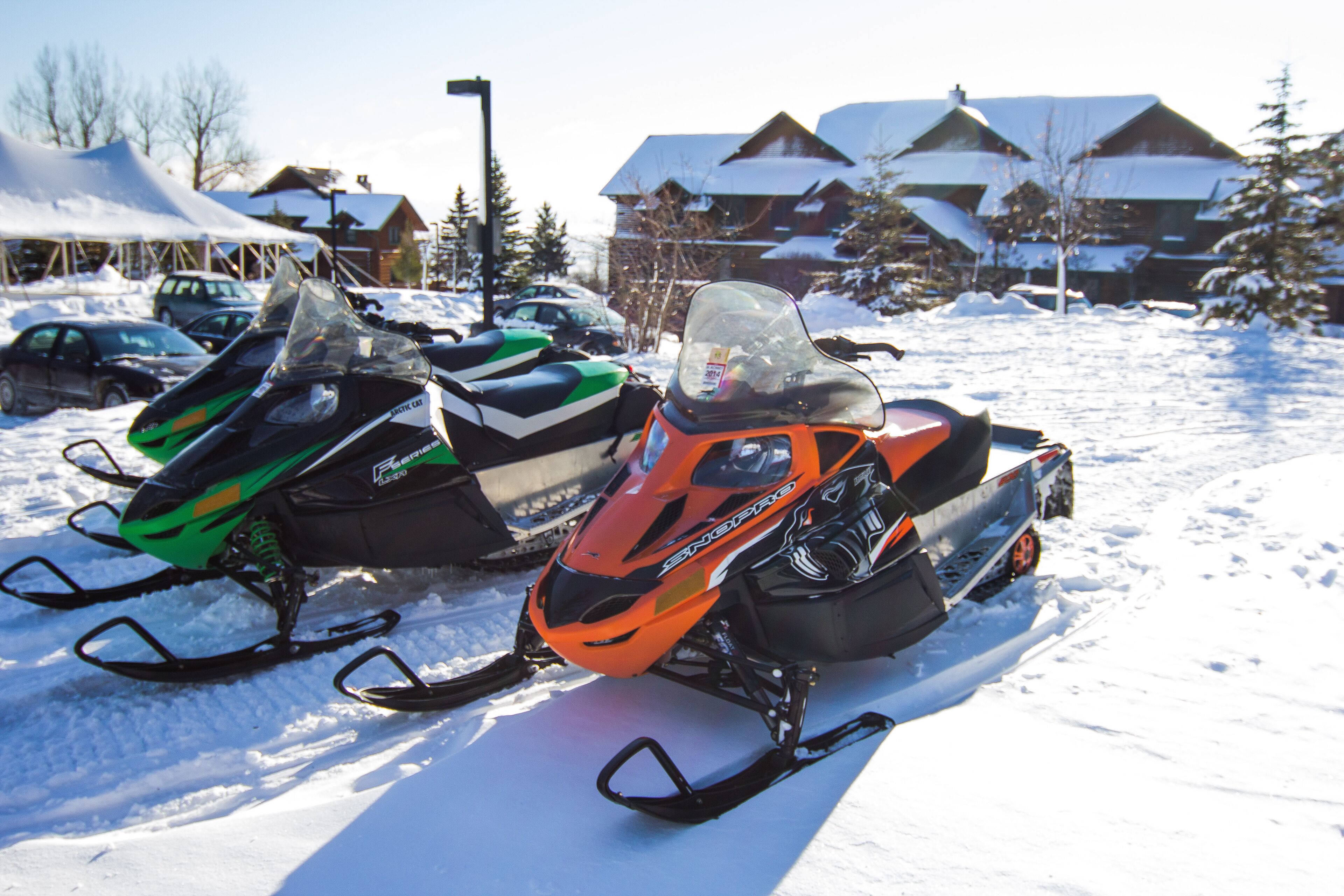 Two snowmobiles parked in a snowy area with buildings in the background.