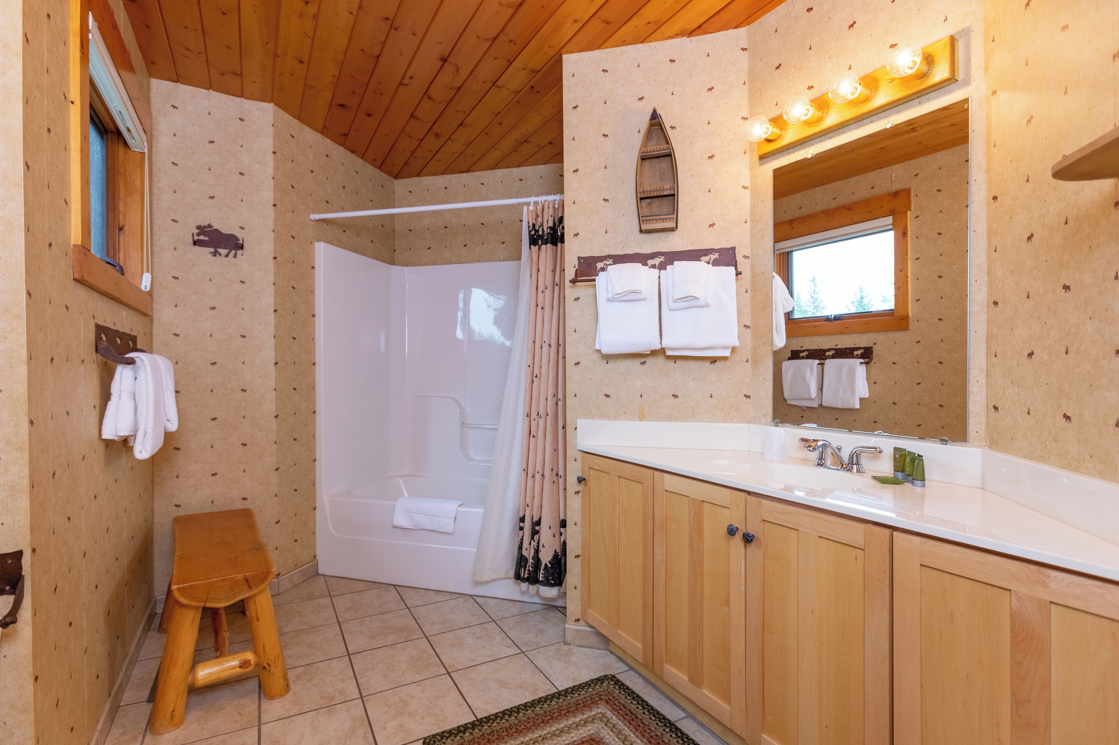 Ein Badezimmer mit Holzboden, einer Badewanne, einer Dusche, Holzschränken und einem beleuchteten Spiegel.