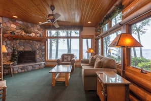 A cozy cabin interior with a stone fireplace, wooden furniture, and large windows offering a view of the lake.