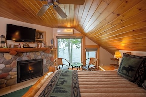 A cozy room with a fireplace, a television, a bed with a patterned blanket, and a view of the outdoors.