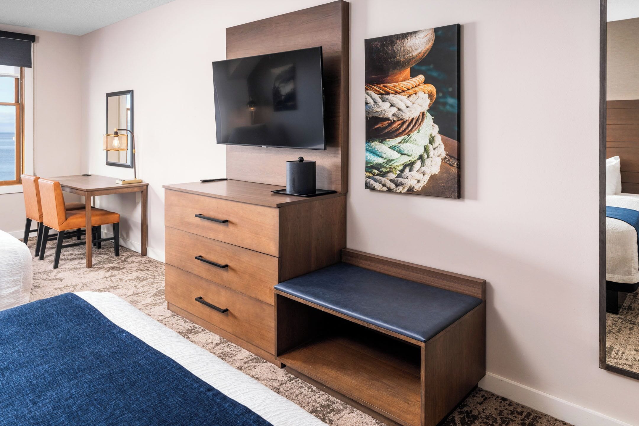 Een hotelkamer met een bed, een bureau, een televisie, een kast en kunst aan de muur.
