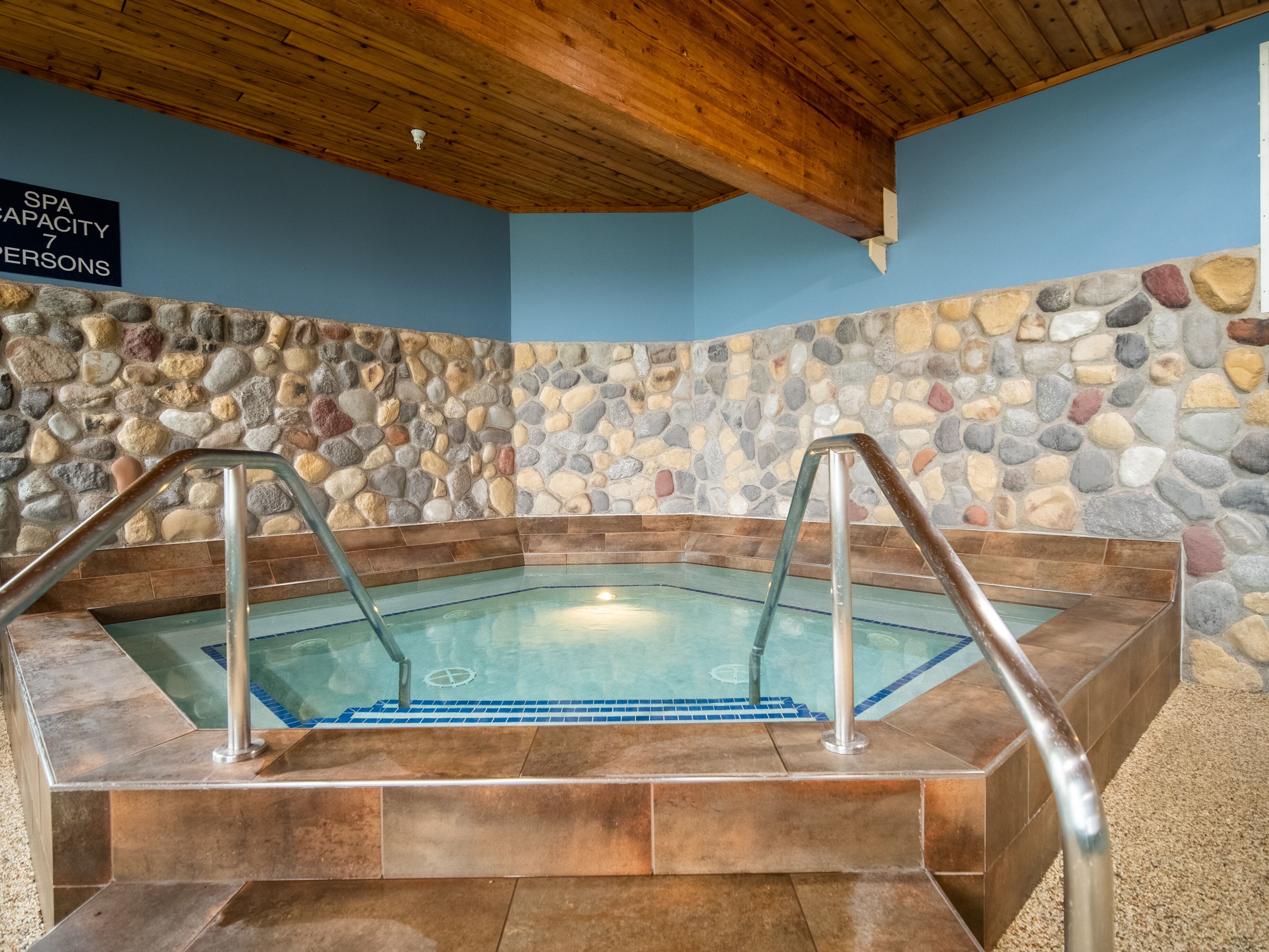A spa with a capacity of 7 persons, a stone wall, and a wooden ceiling.