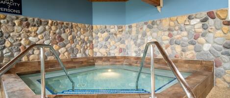 Un spa con capacidad para 7 personas, pared de piedra y techo de madera.