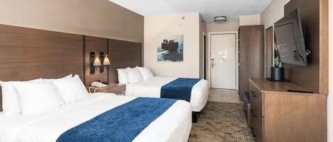 A hotel room with two beds, a desk, a television, and a painting on the wall.