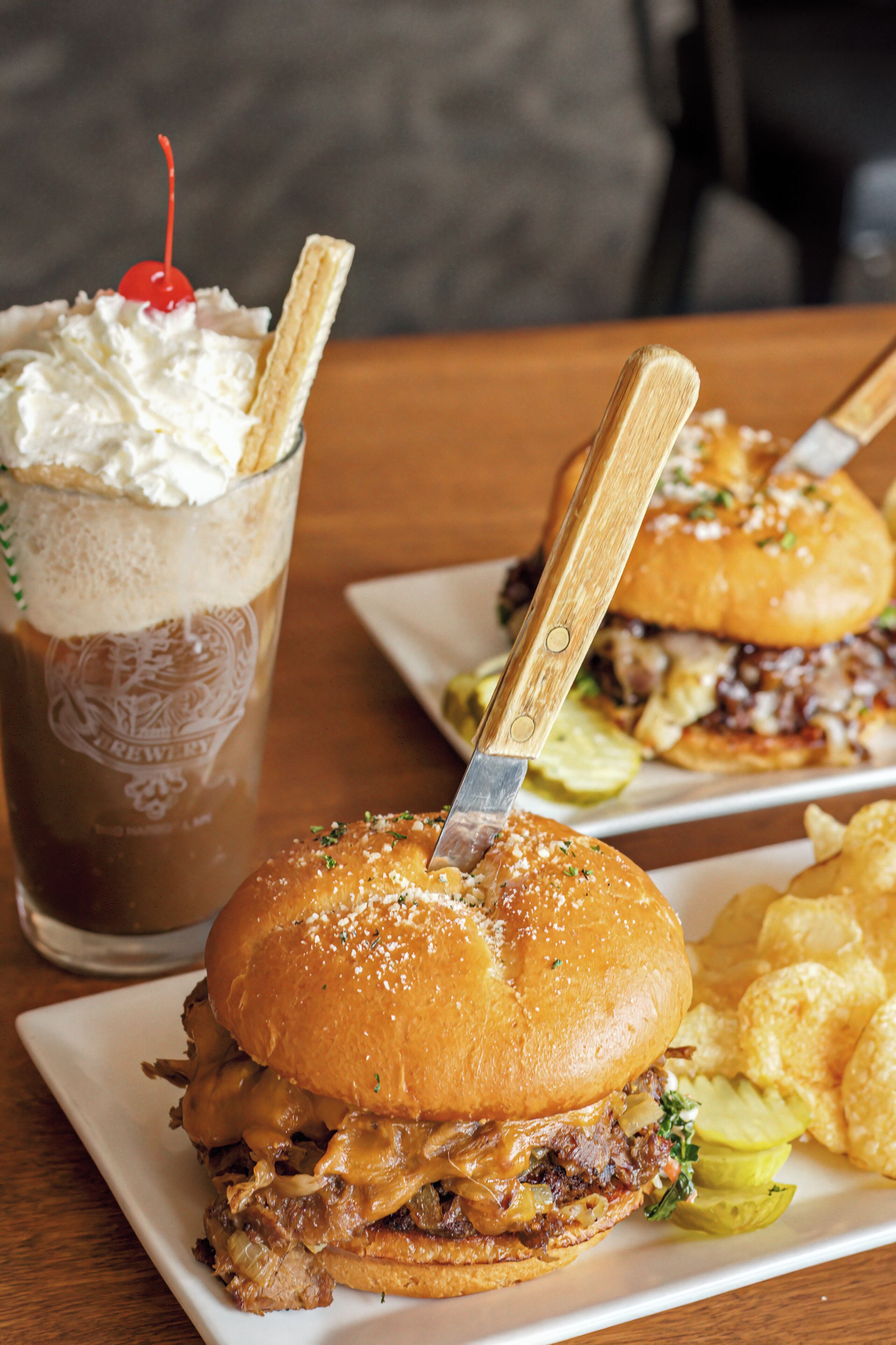 Un sándwich, un tenedor, una bebida con crema batida y cereza, y papas fritas en un plato.