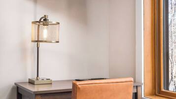 Une chambre dotée d’un téléviseur à écran plat fixé au mur, d’un bureau avec une lampe, d’une chaise et d’une fenêtre donnant sur des arbres.