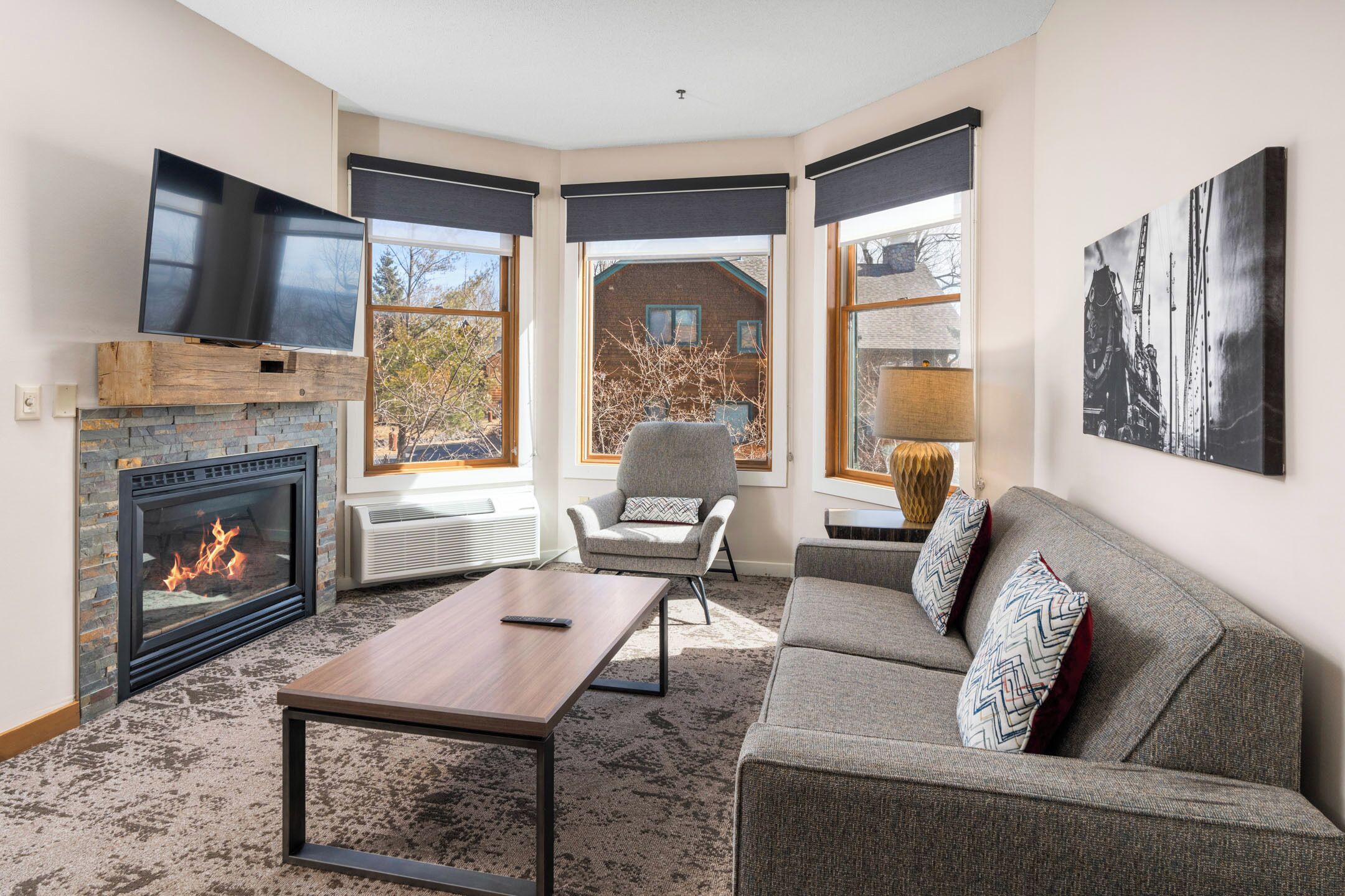 A living room with a fireplace, a sofa, a TV, and large windows.