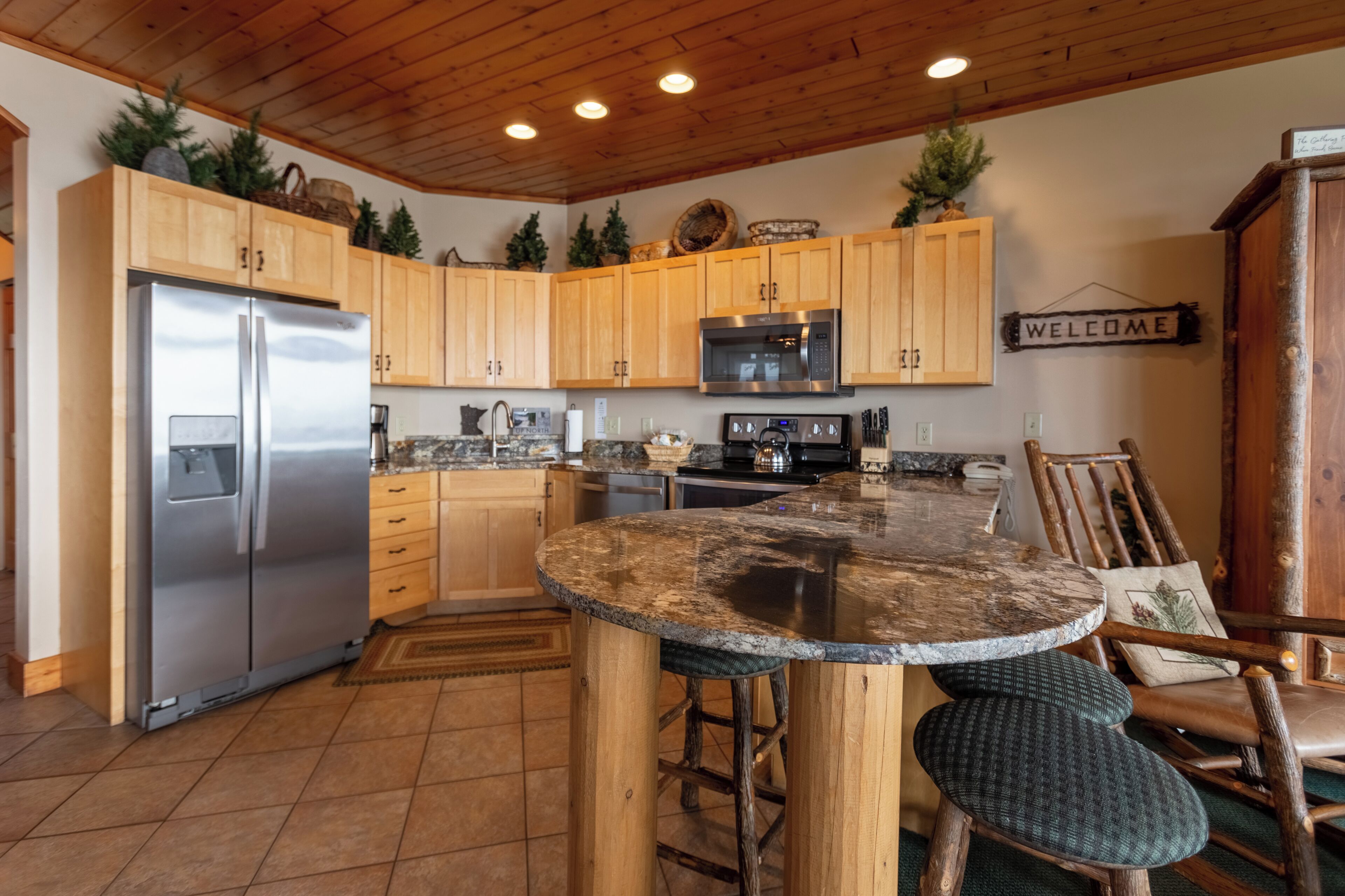 A kitchen with wooden cabinets, a stainless steel refrigerator, a microwave, and a welcome sign.