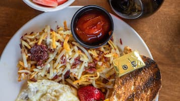 Une assiette de petit-déjeuner comprenant des toasts, des œufs brouillés, des pommes de terre rissolées et un saladier de fruits contenant des fraises, des myrtilles et de la pastèque.