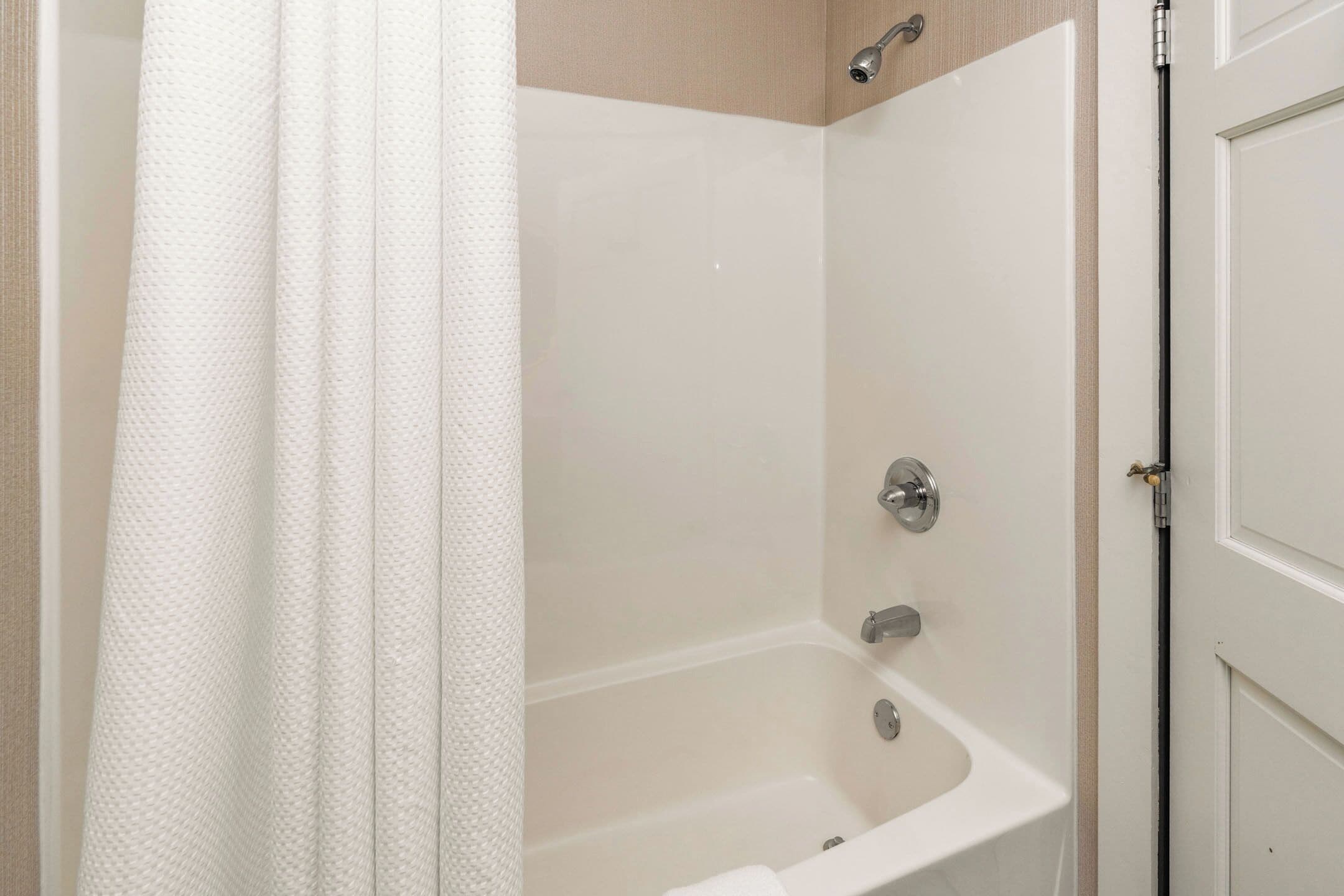 A bathroom with a bathtub, a shower curtain, and a door.