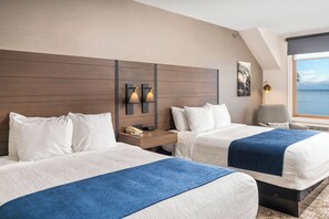 A hotel room with two beds, a nightstand with a phone, wall-mounted lights, a chair, and a large window with a view of the sea. - Grand Superior Lodge (Two Harbors)