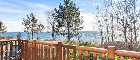 A wooden deck with a chair, overlooking a body of water and trees.