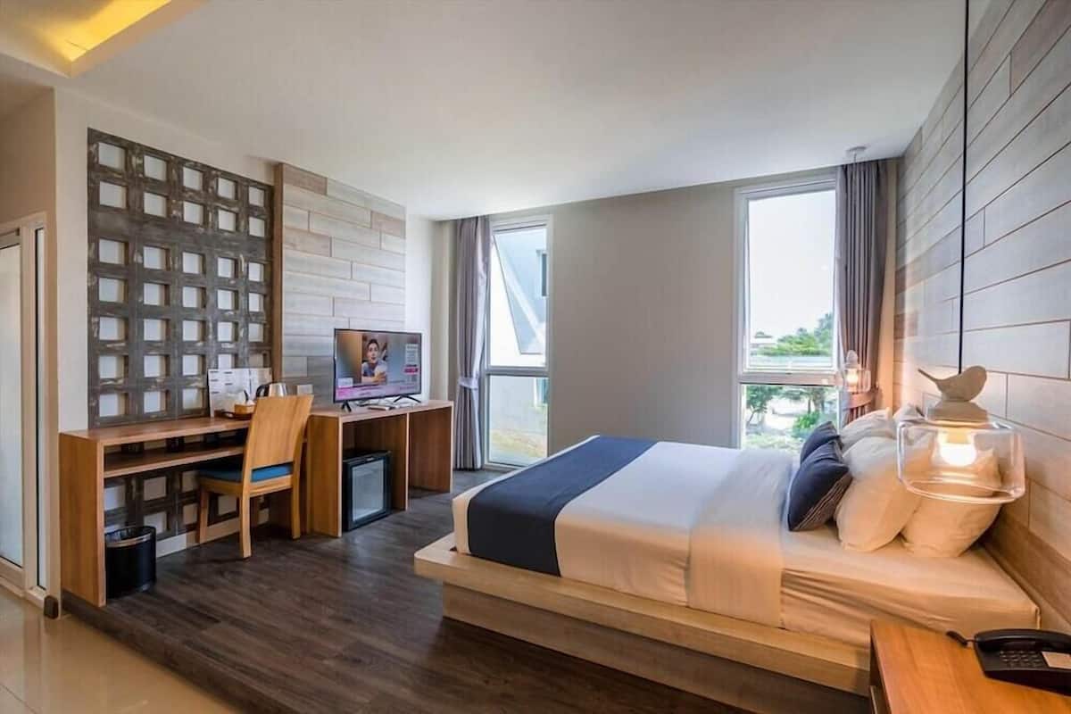 A modern hotel room with a bed, desk, chair, TV, and a view of the outdoors.