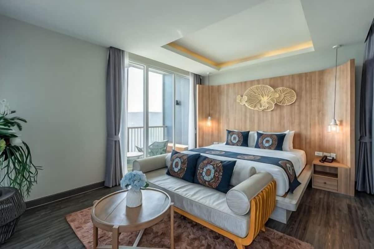 A modern hotel room with a large bed, a sofa, a small table, and a balcony view.